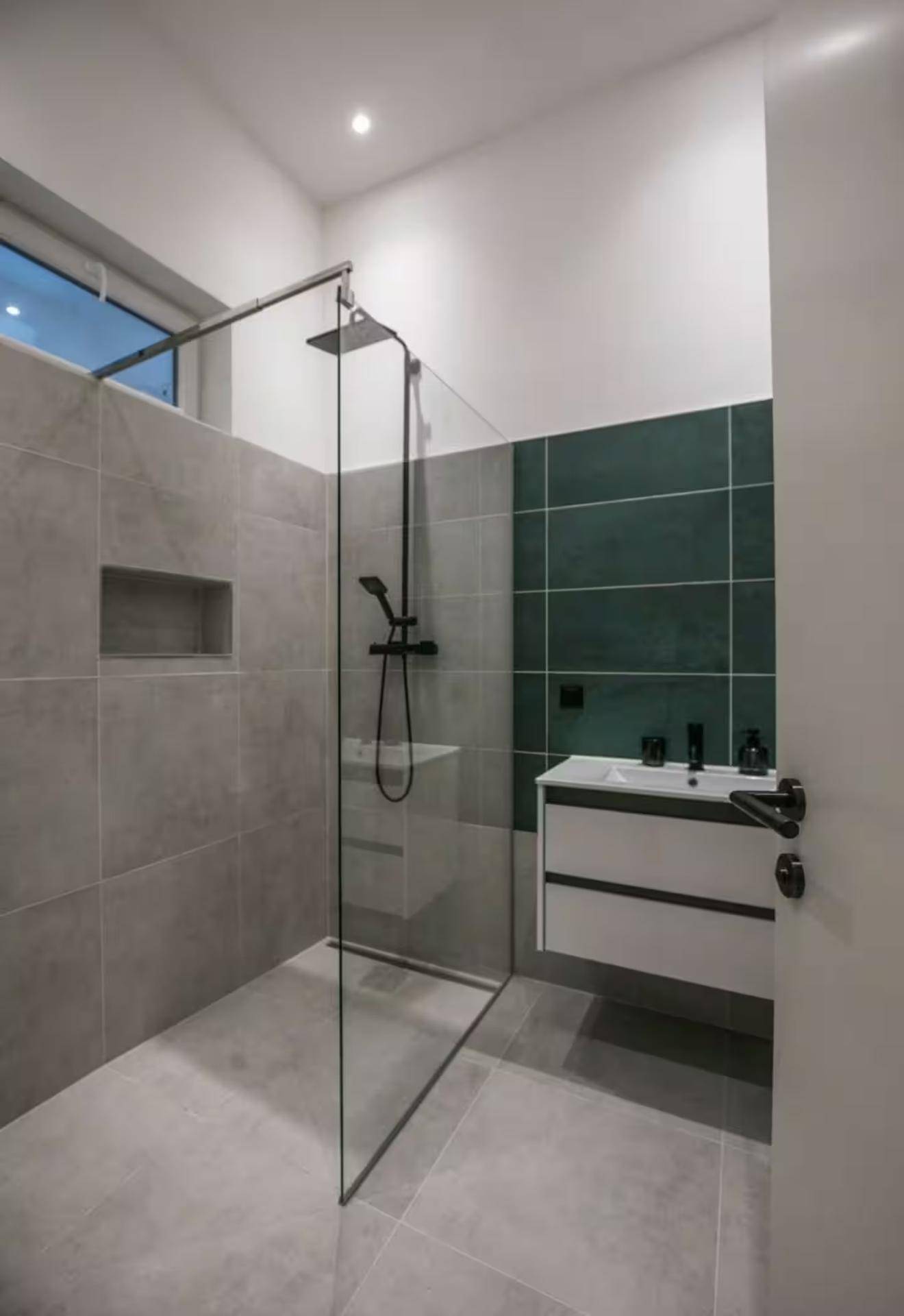 Modernes Badezimmer mit begehbarer Dusche, Einzelwaschbecken und stilvollen Fliesen in Grau und Dunkelgrün.
