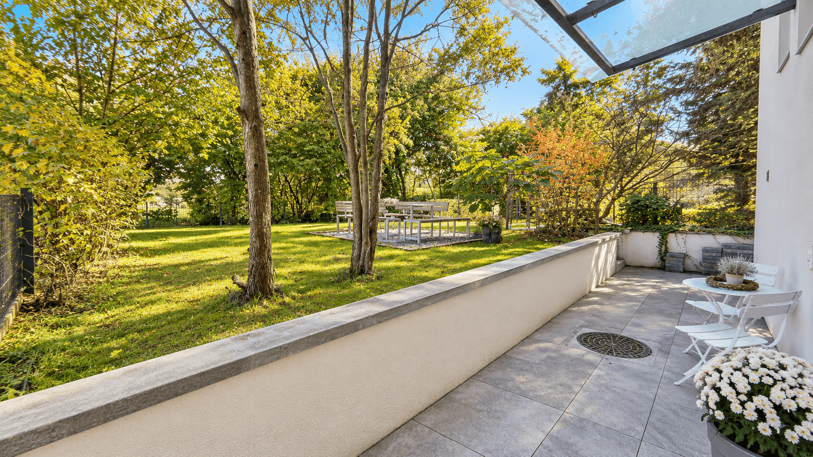 Großer Garten mit Rasenfläche, alten Bäumen und einer gepflasterten Terrasse.