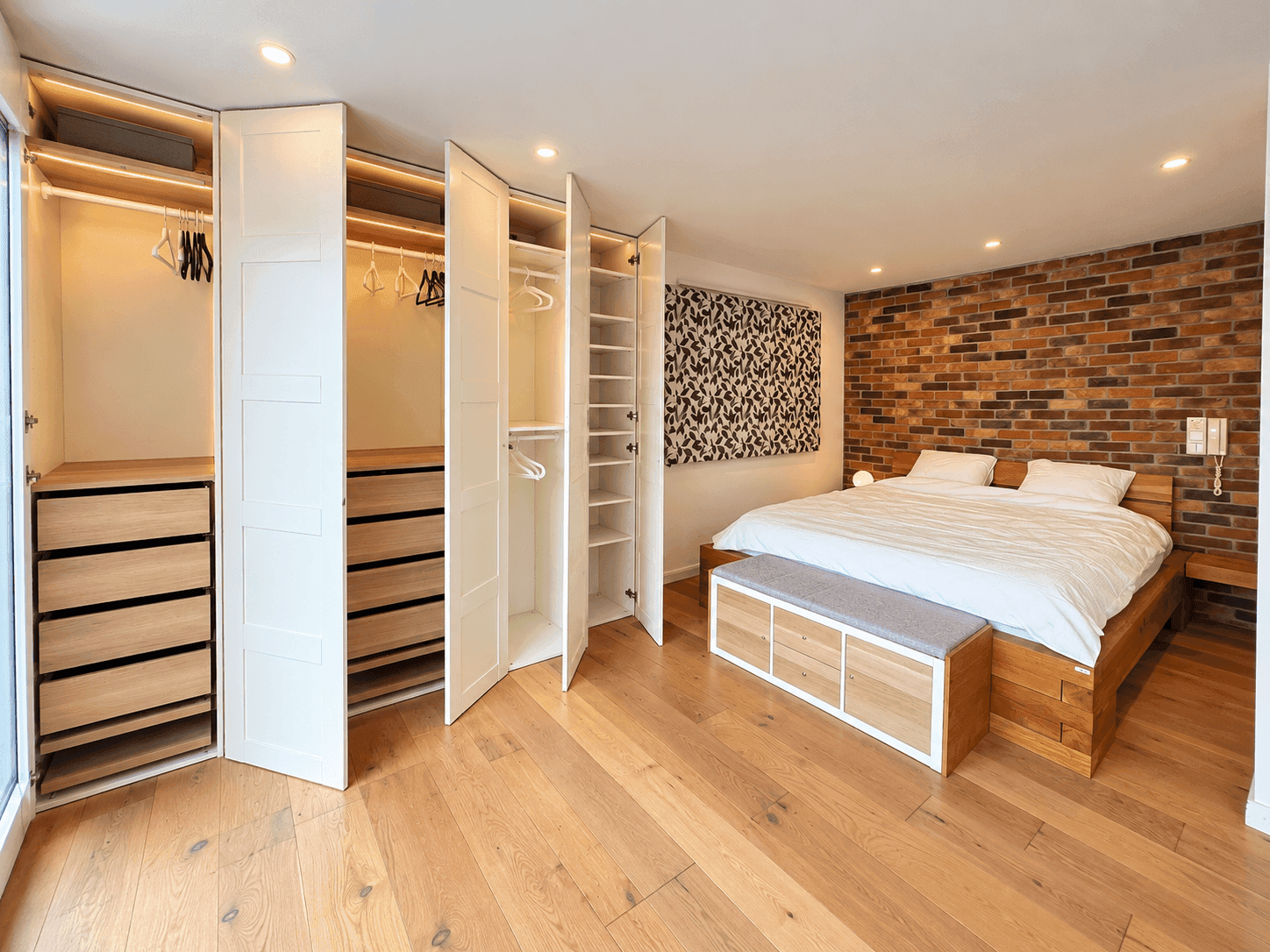 Gemütliches Schlafzimmer mit Holzboden, freigelegter Ziegelwand und integrierten Kleiderschränken.