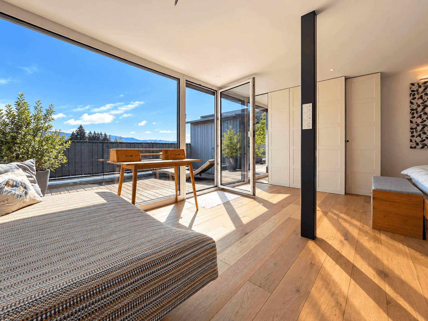 Helles Zimmer mit Holzboden, großen Glasfronten und Zugang zu einer sonnigen Terrasse mit Bergblick.