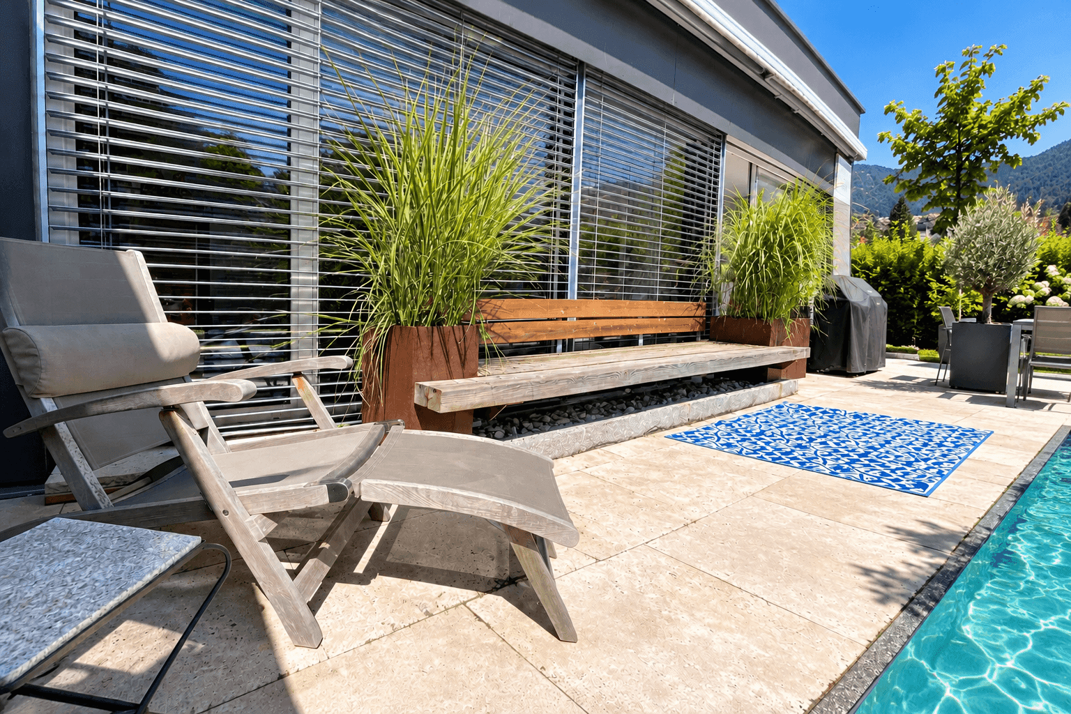 Sonniger Terrassenbereich am Pool mit Liegestühlen und großen Fenstern.