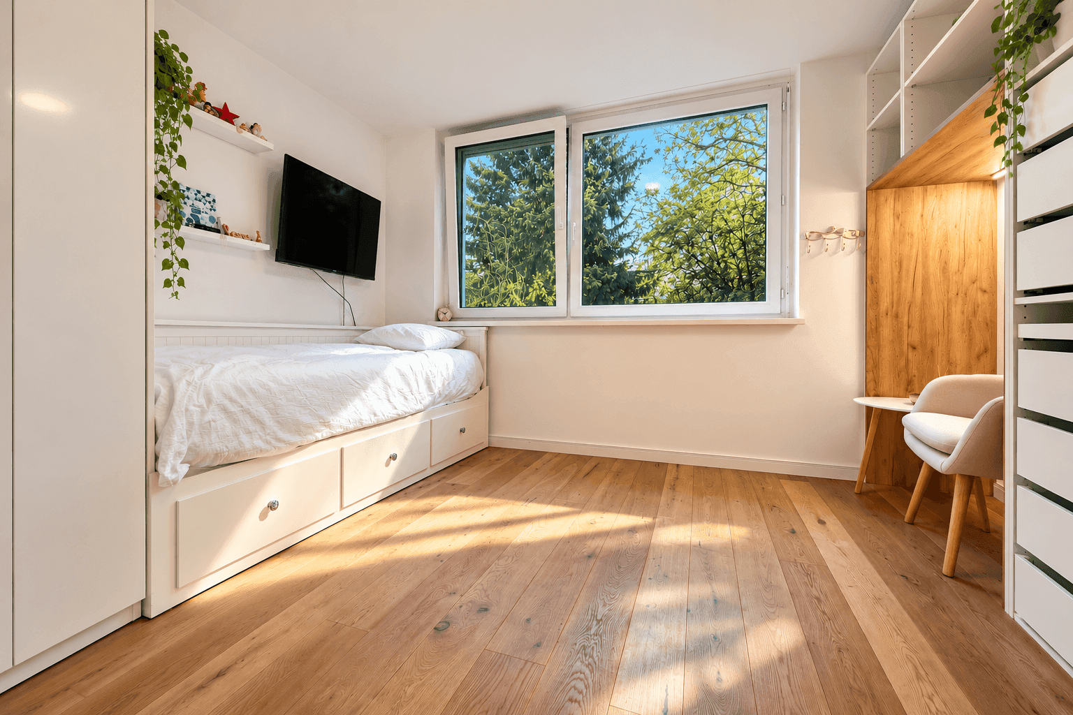 Helles Schlafzimmer mit Holzboden, weiß gestrichenen Wänden und Blick ins Grüne.