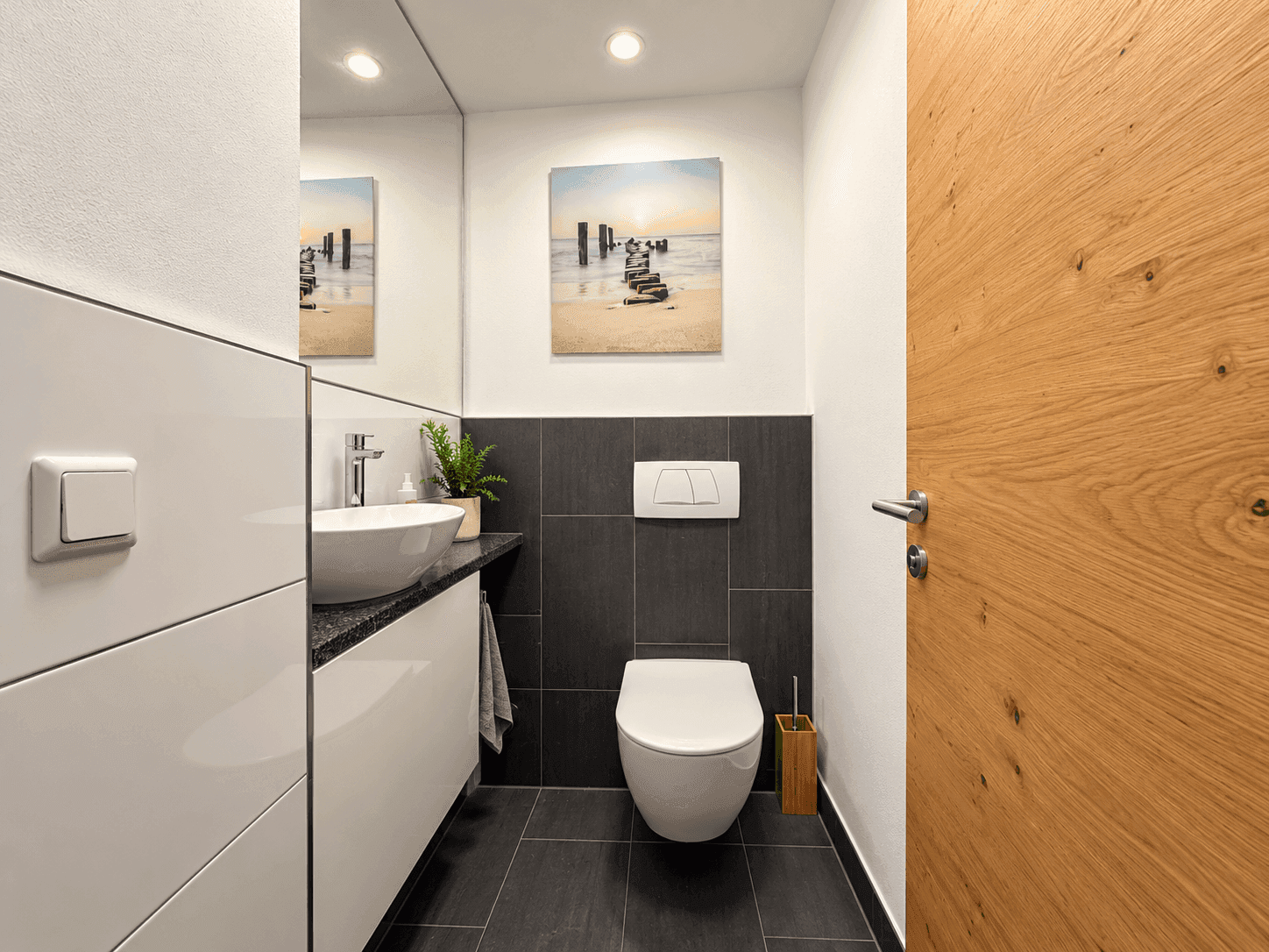Modernes Gäste-WC mit wandhängender Toilette, stilvollem Waschbecken und dunklen Fliesen.