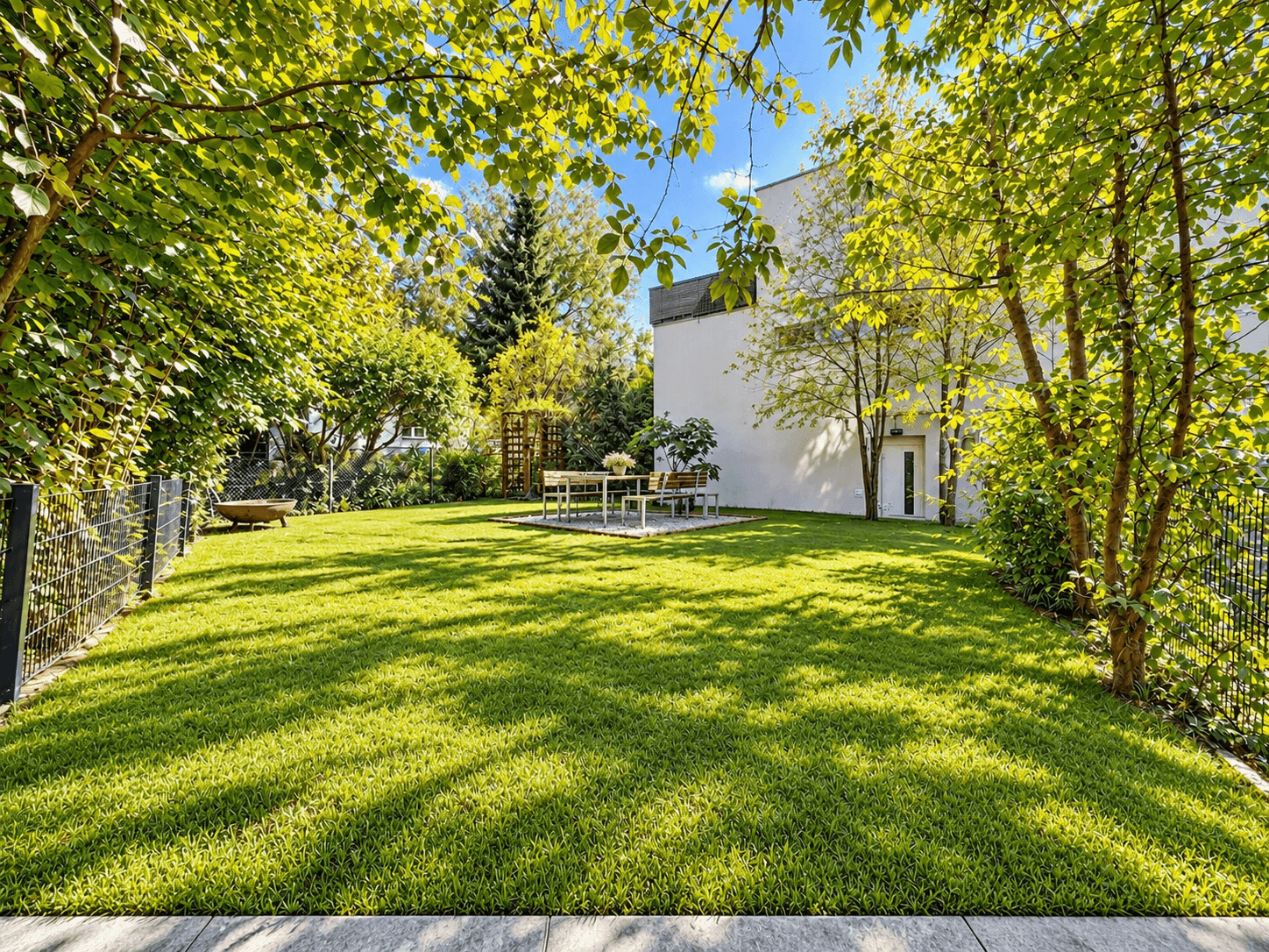 Großer, gepflegter Garten mit Rasenfläche und Essbereich unter schattenspendenden Bäumen.