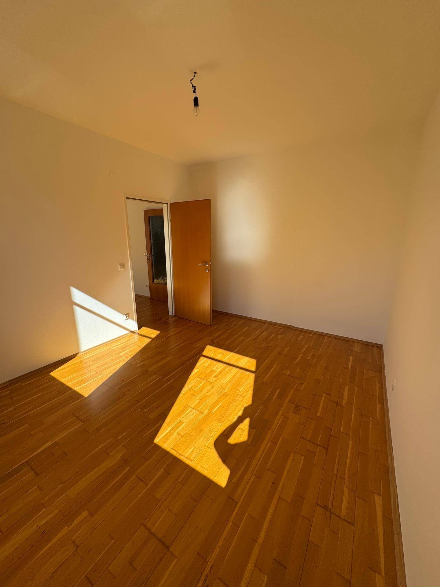 Leeres Zimmer mit Parkettboden und Holztür, bereit für neue Bewohner und Einrichtung.