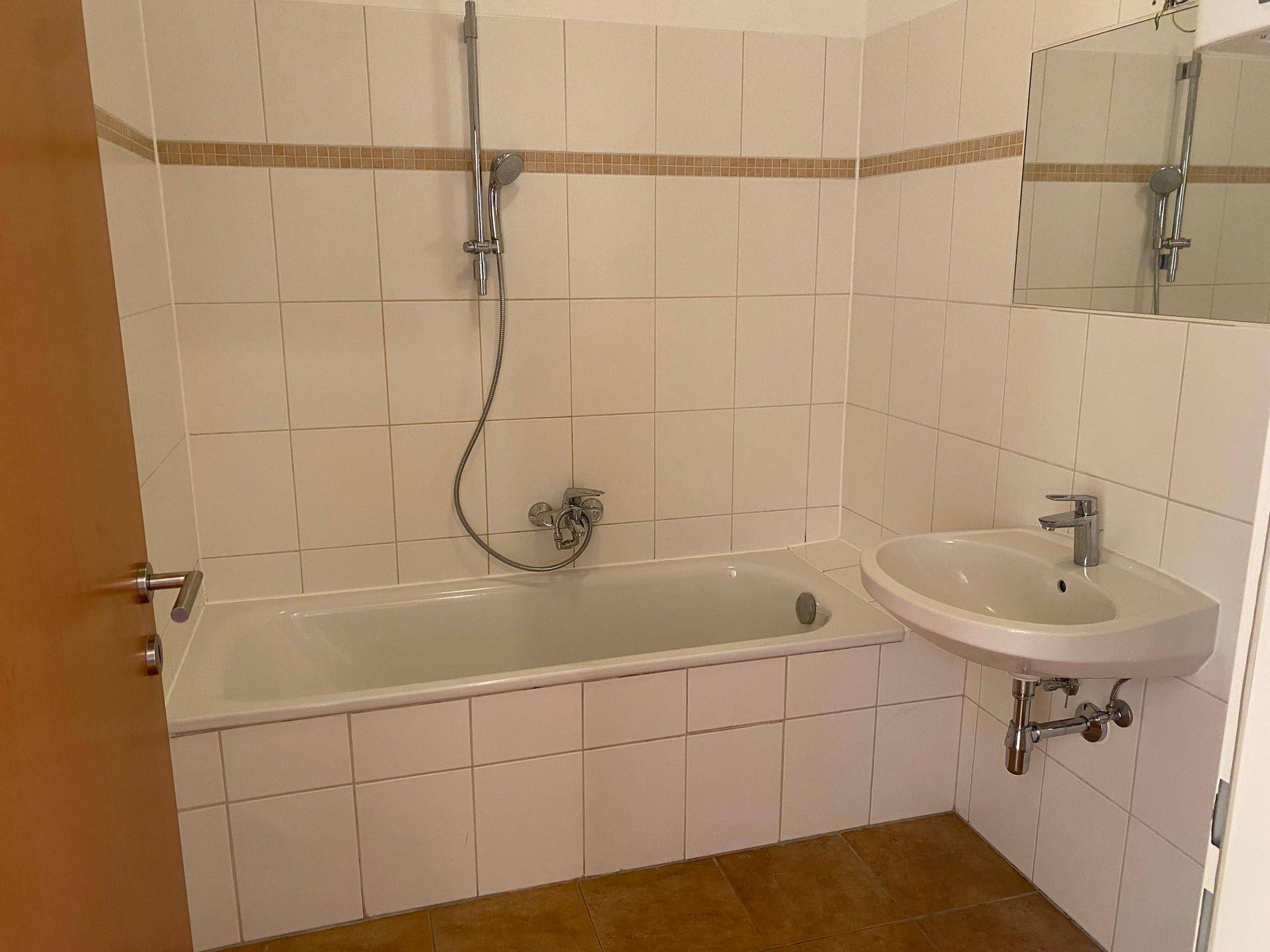 Badezimmer mit Badewanne, Waschbecken und hellen Fliesen, bereit zur Nutzung.