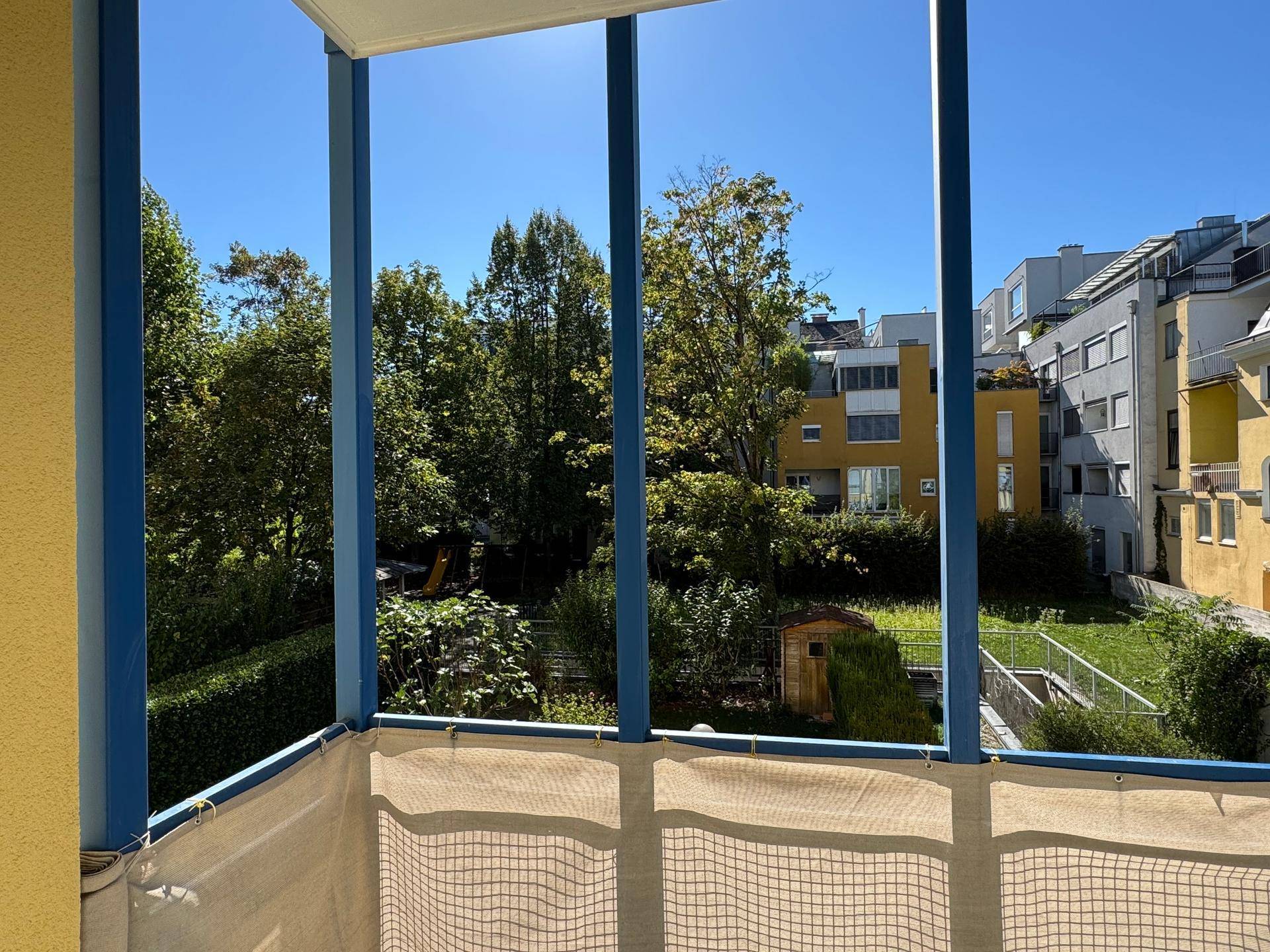 Sonniger Balkon mit Blick ins Grüne und auf die umliegenden Gebäude.