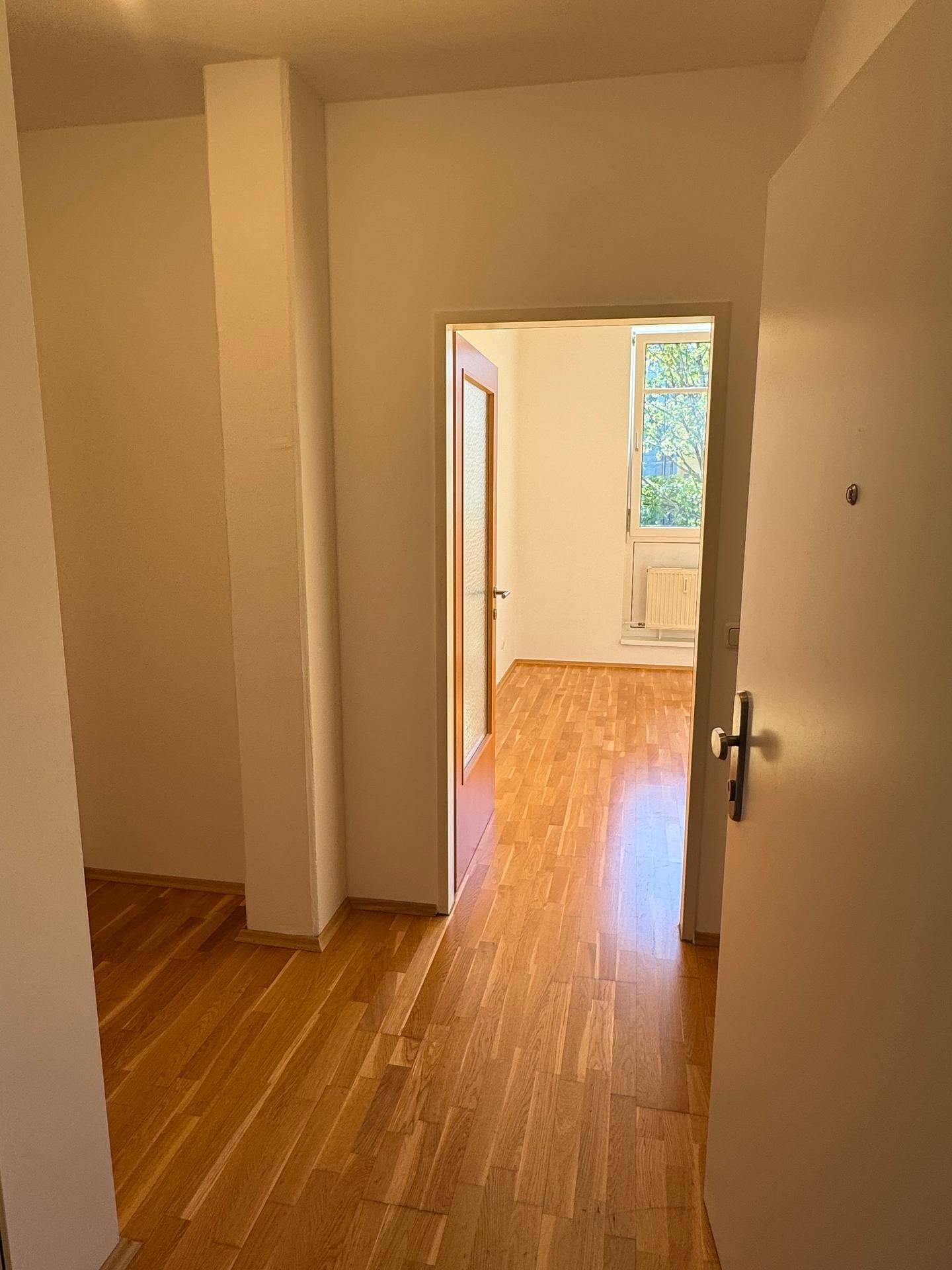 Flur mit Parkettboden und Blick in ein helles Zimmer, das viel Tageslicht erhält.