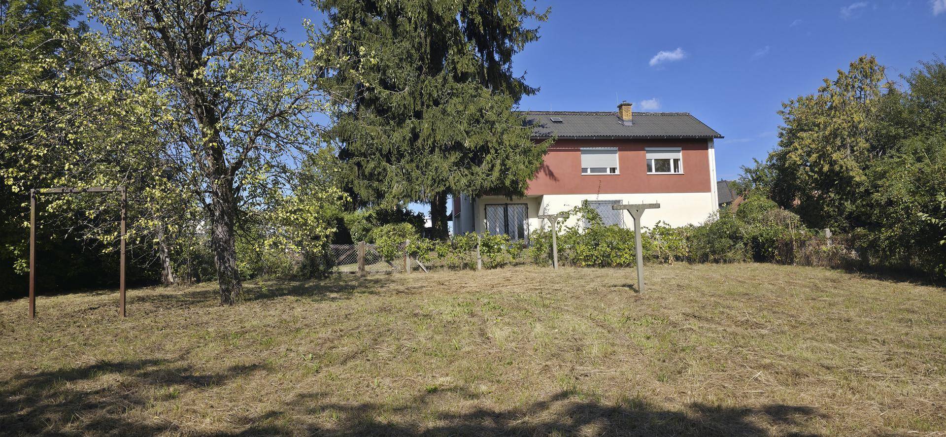 Haus mit roter Fassade und einem großen, naturbelassenen Gartenbereich mit Bäumen und Wiese.