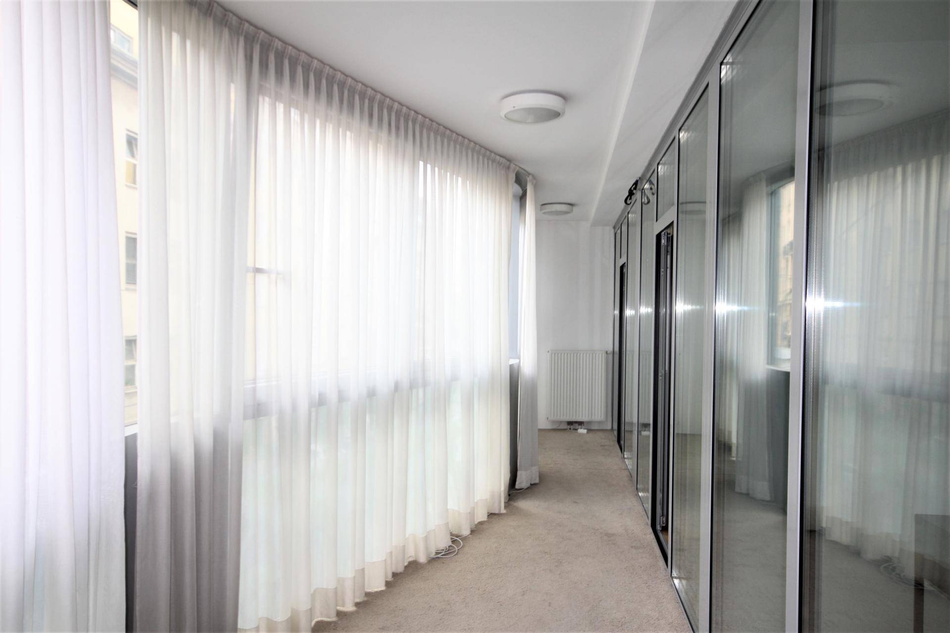 Heller Flur mit großen Fenstern, transparenten Vorhängen und reflektierenden Glaswänden.