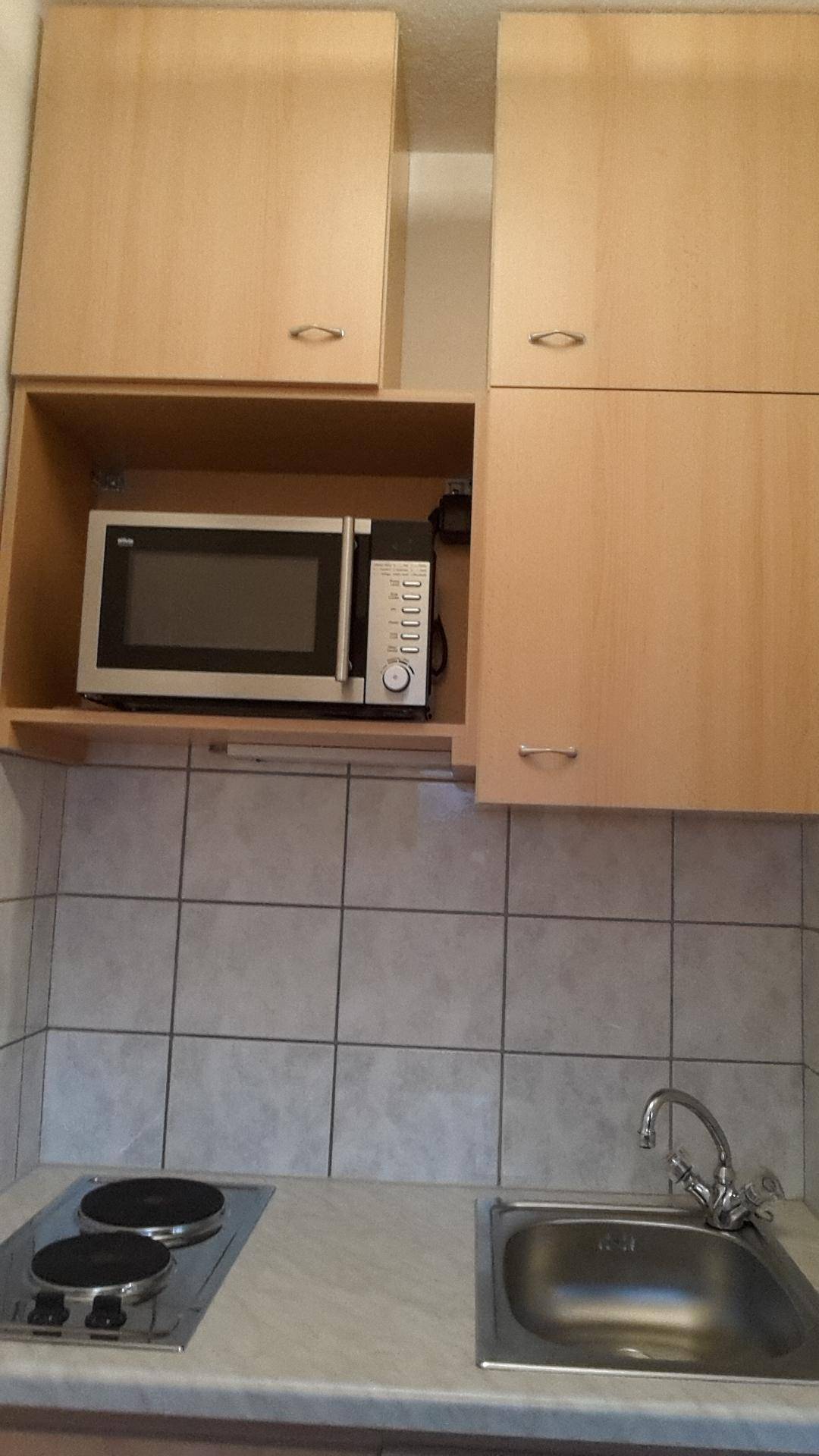 Kleine Küchenzeile mit Holzschränken, Mikrowelle und Kochfeld.