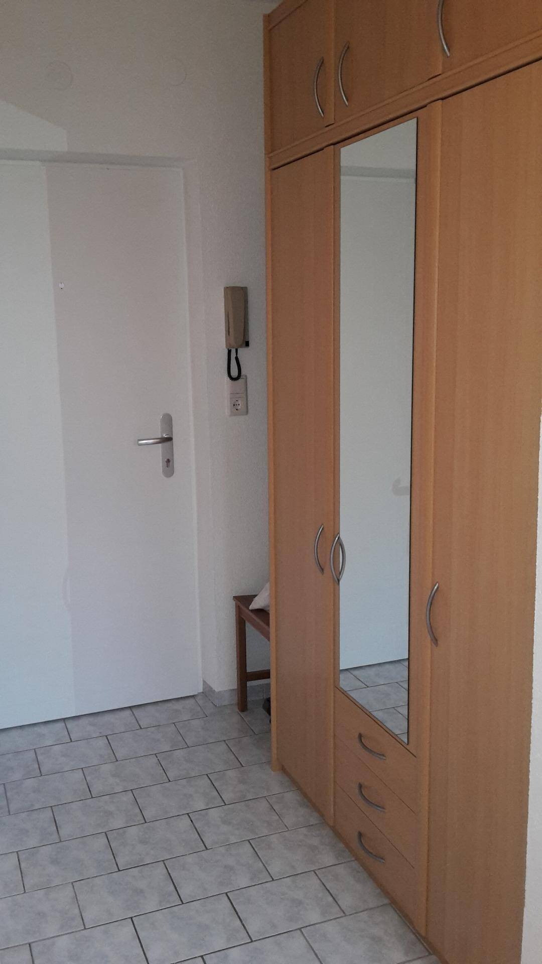 Heller Flur mit Spiegelschrank und weißer Tür auf Fliesenboden.