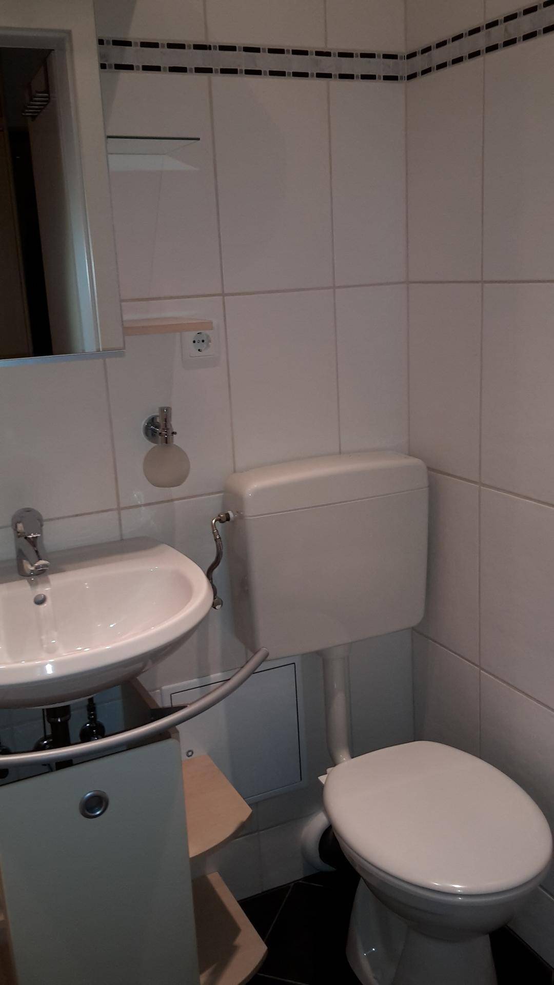 Kleines Badezimmer mit WC, Waschbecken und weißen Wandfliesen.