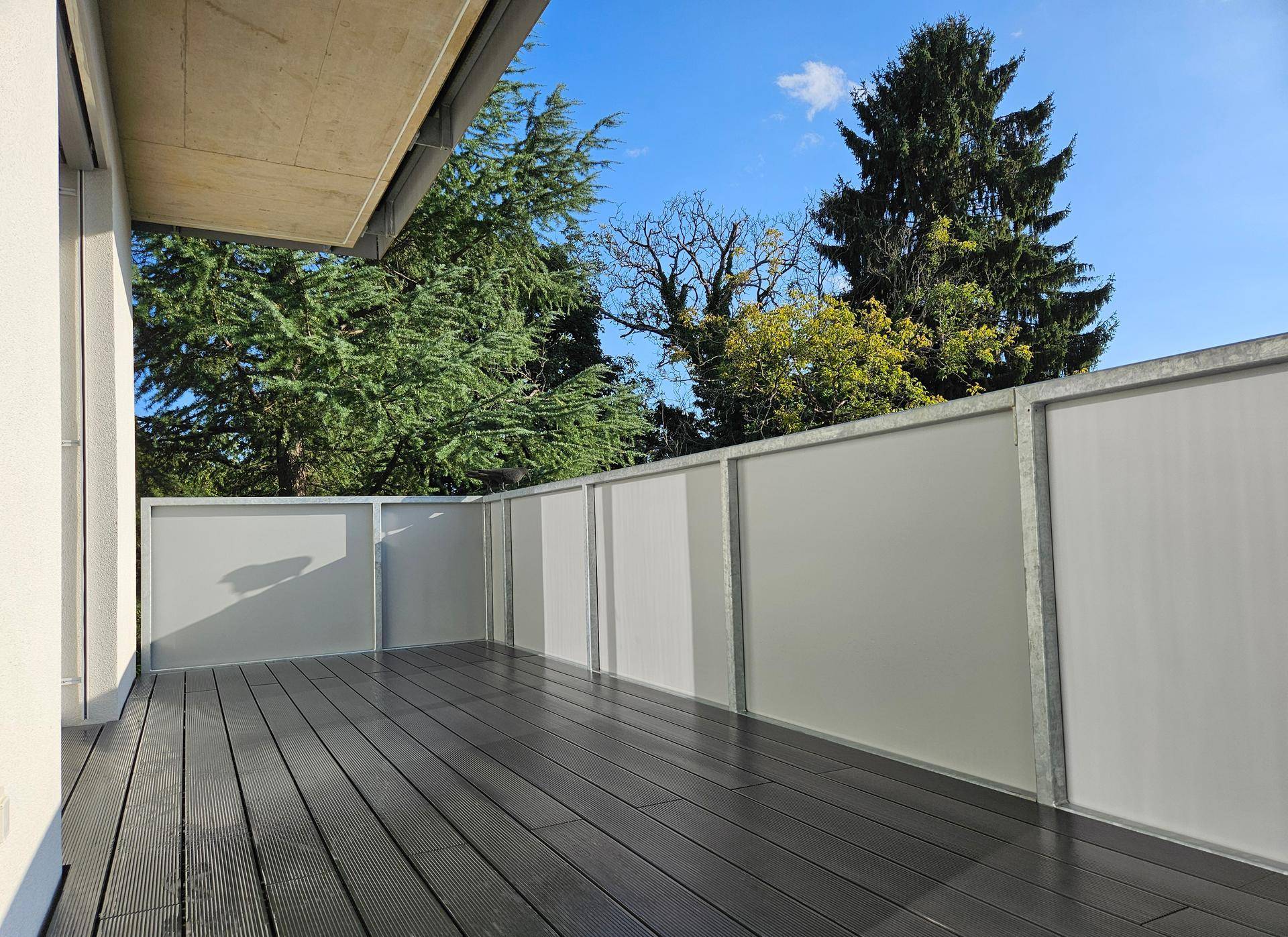 Geräumiger Balkon mit modernen WPC-Dielen und einer blickdichten Brüstung, umgeben von Bäumen.