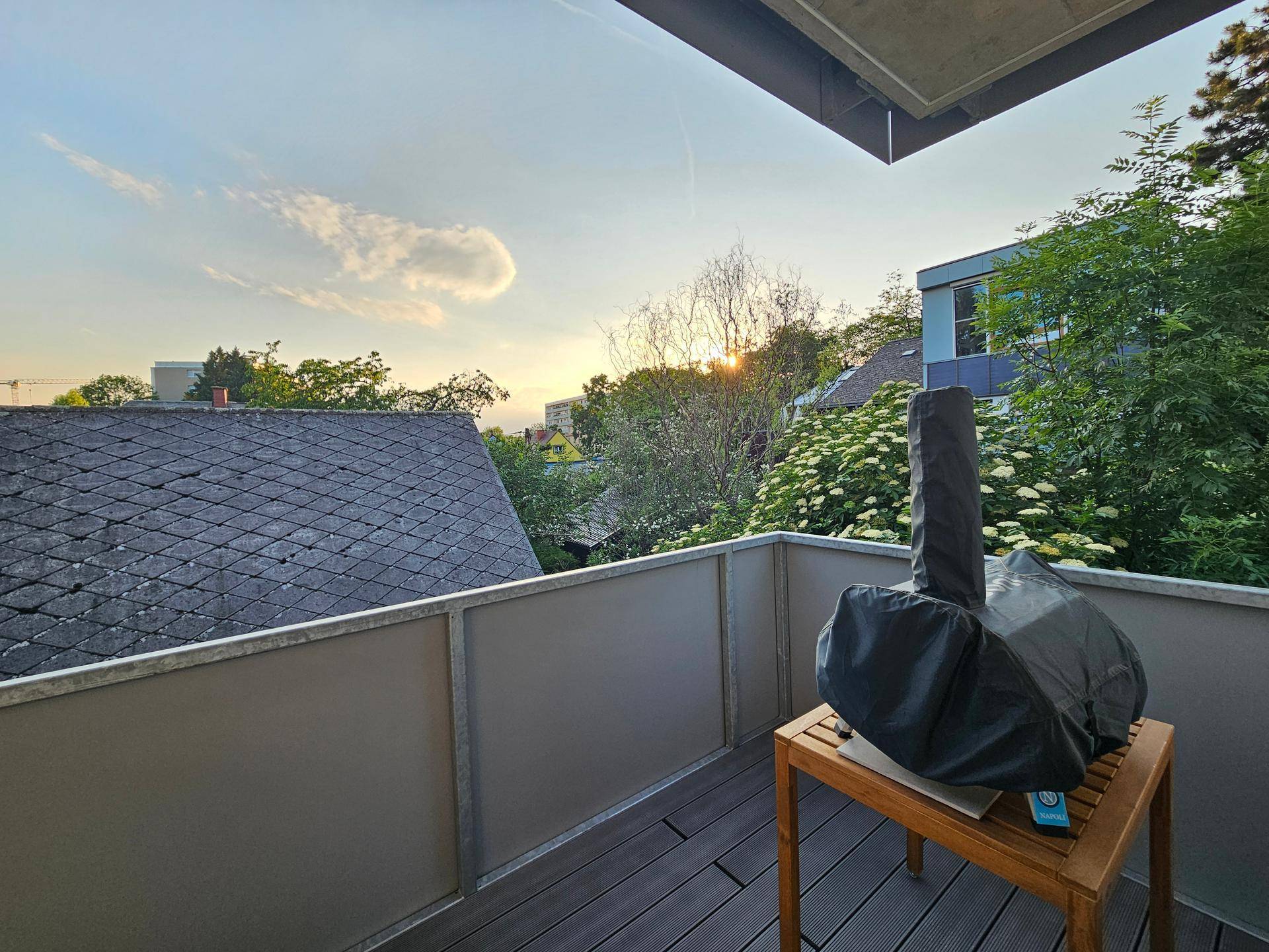 Balkon mit einem Grill und Blick über die Dächer bei Sonnenuntergang.