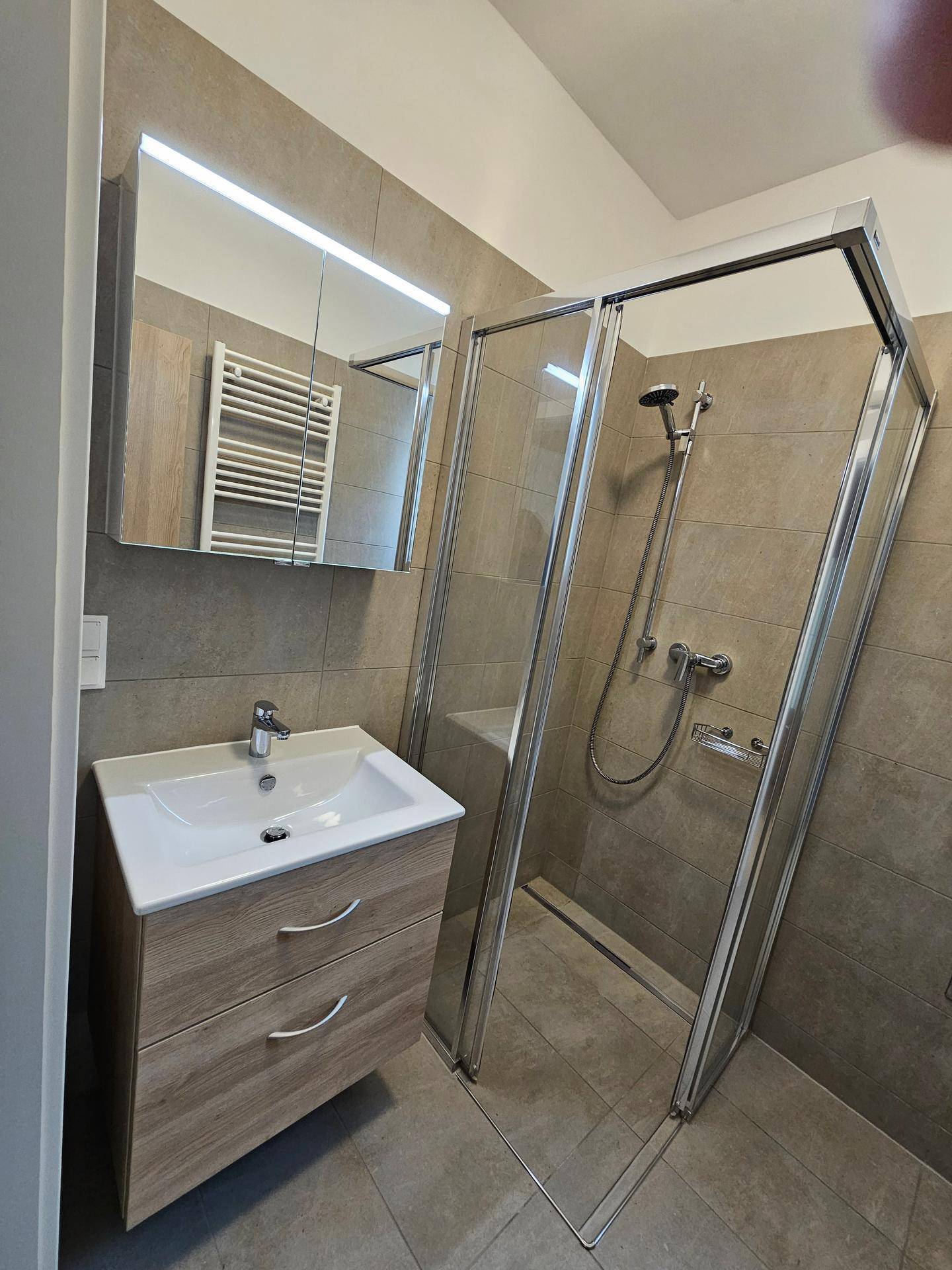 Modernes Badezimmer mit begehbarer Dusche, Waschtisch und beheiztem Handtuchhalter.