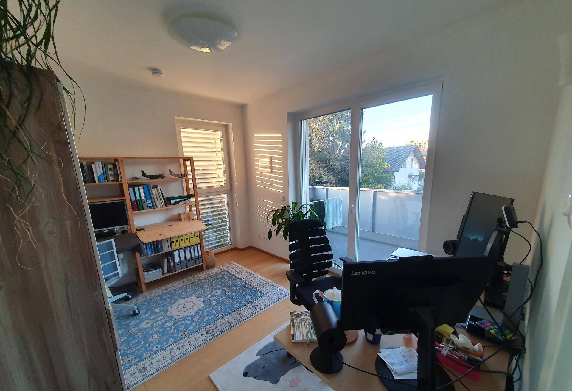 Sonniges Arbeitszimmer mit Schreibtisch, Bücherregal und Zugang zu einem Balkon.