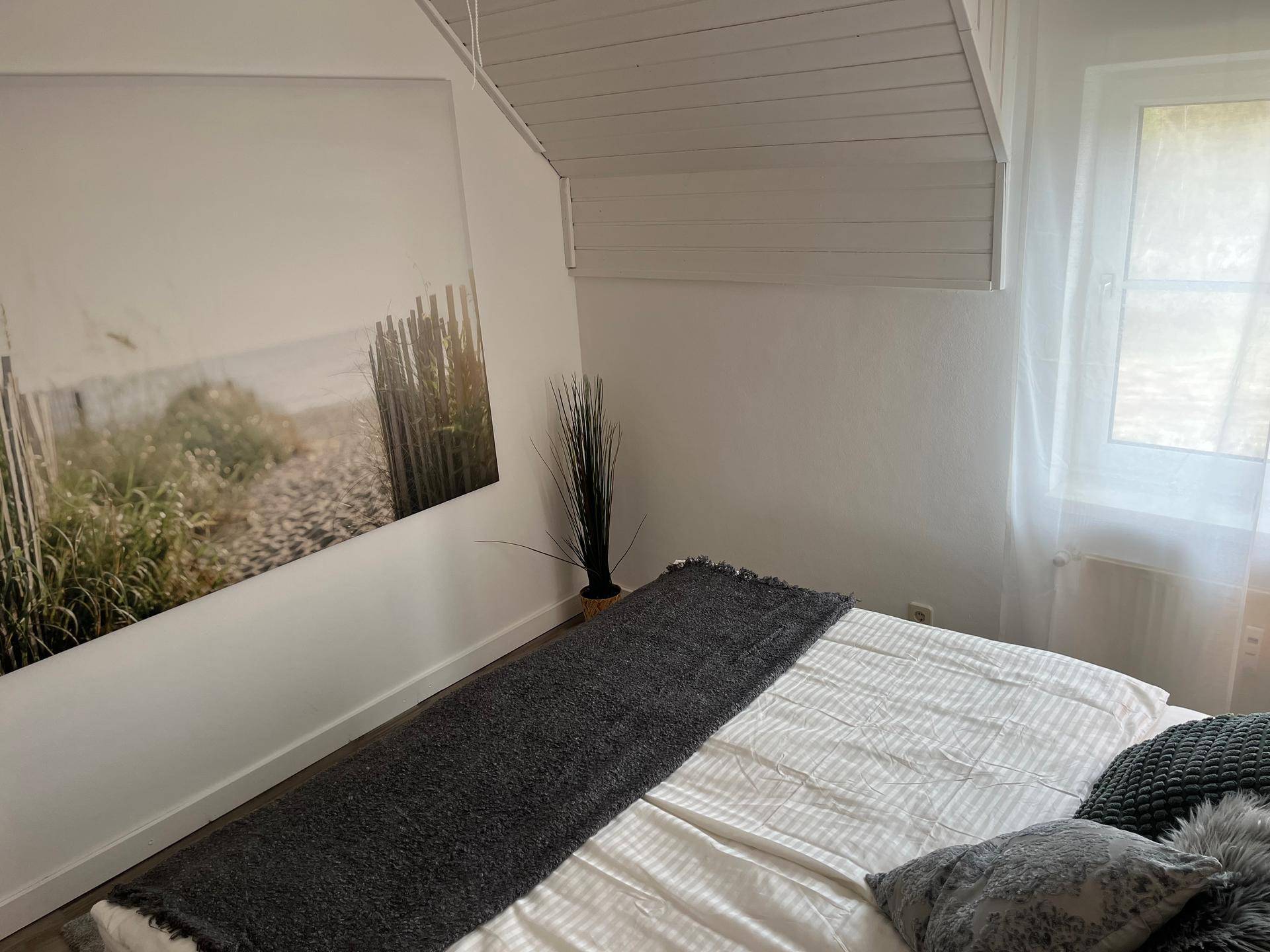 Schlafzimmer mit Dachschräge, Doppelbett und einem Bild mit Strandmotiv an der Wand.