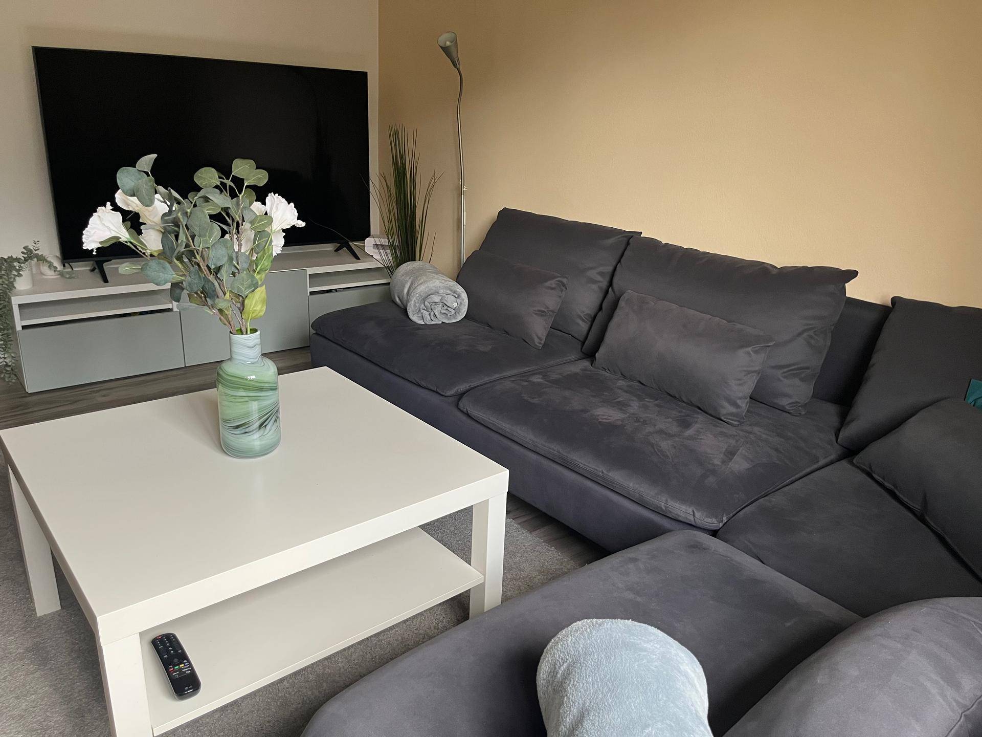 Komfortables Wohnzimmer mit großem Ecksofa, Flachbildfernseher und heller Wandfarbe.