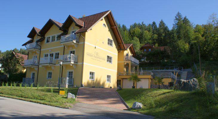 Attraktives gelbes Mehrfamilienhaus mit mehreren Balkonen und einer großen Terrasse im Grünen.