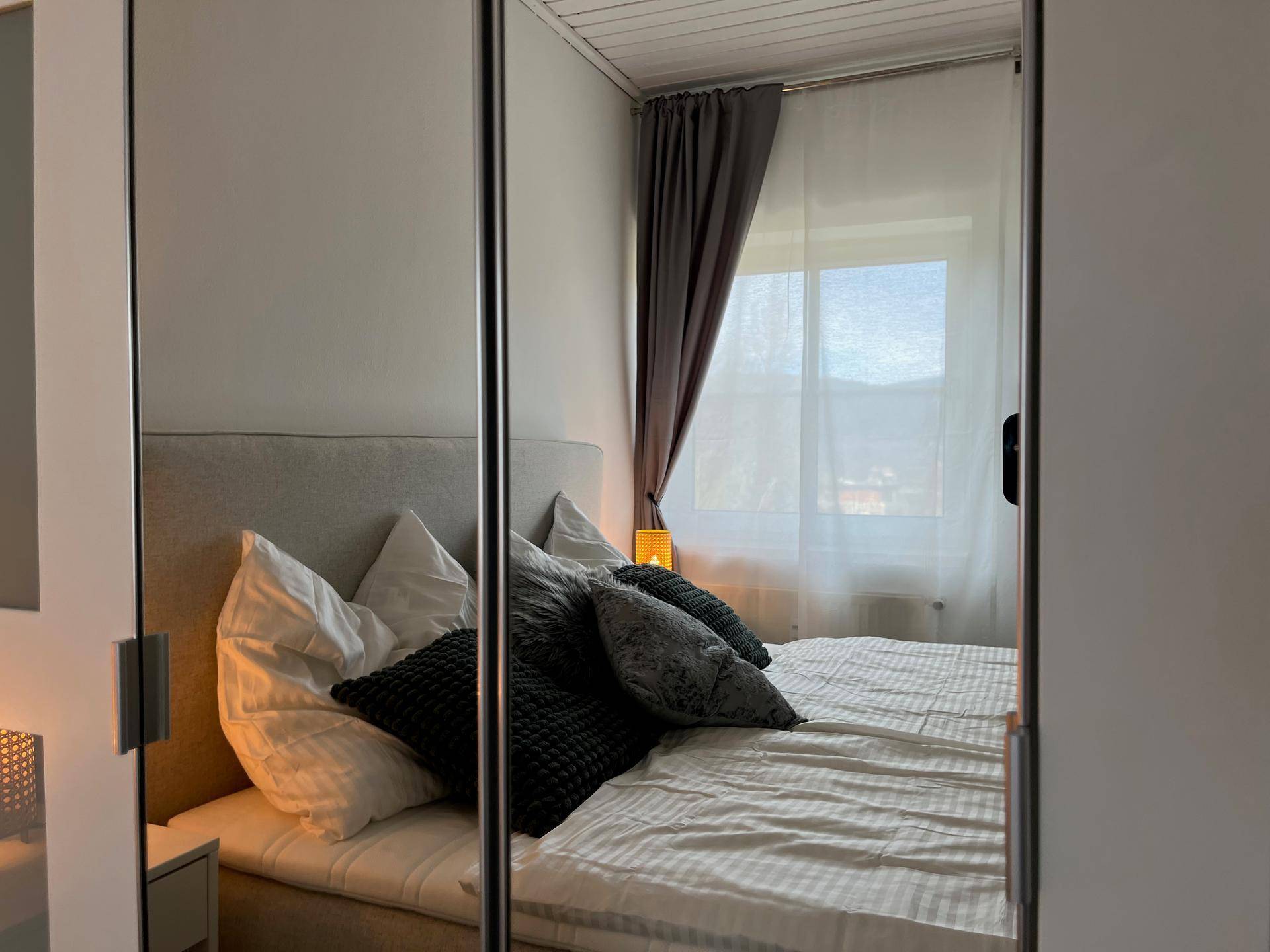 Helles Schlafzimmer mit Doppelbett, Nachttisch und Fenster mit Blick ins Grüne.