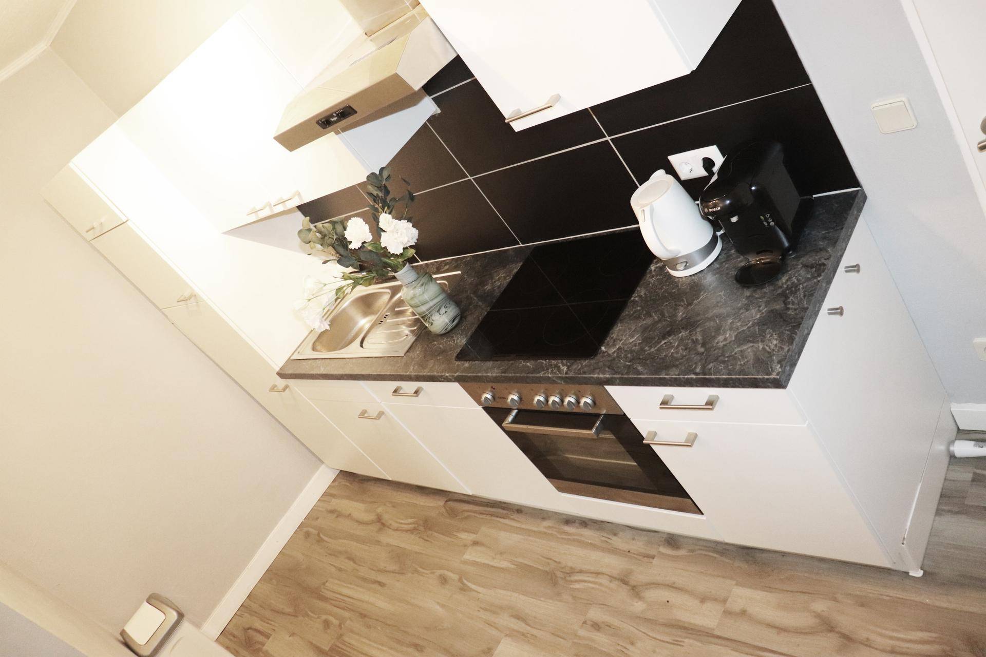 Moderne Küchenzeile mit weißen Schränken, Induktionskochfeld und dunkler Arbeitsplatte.