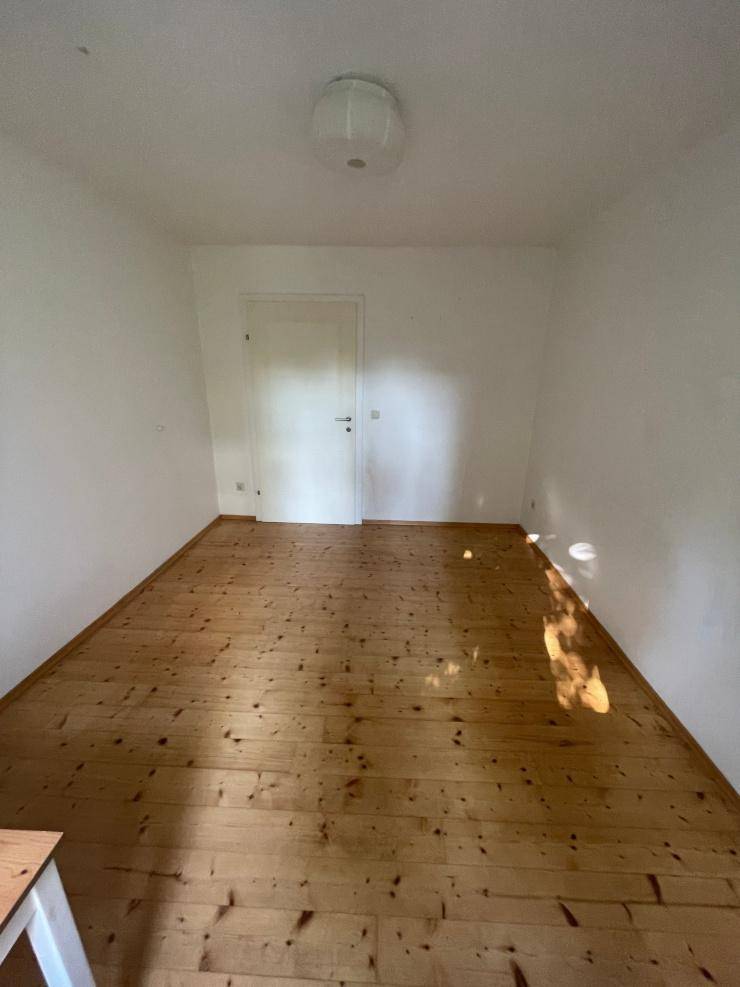Einfaches Zimmer mit Holzdielenboden und weiß gestrichenen Wänden, bereit zur individuellen Gestaltung.