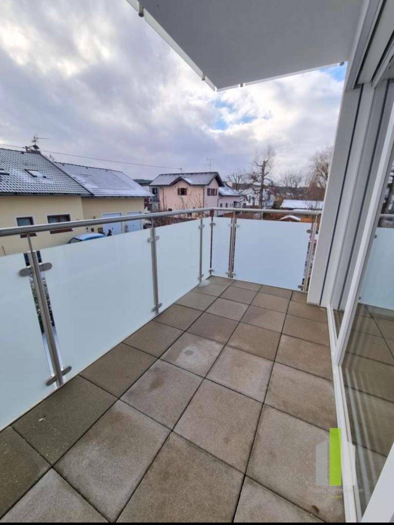 Moderner Balkon mit Glasbrüstung und Fliesenboden, bietet einen Blick auf die verschneite Umgebung.