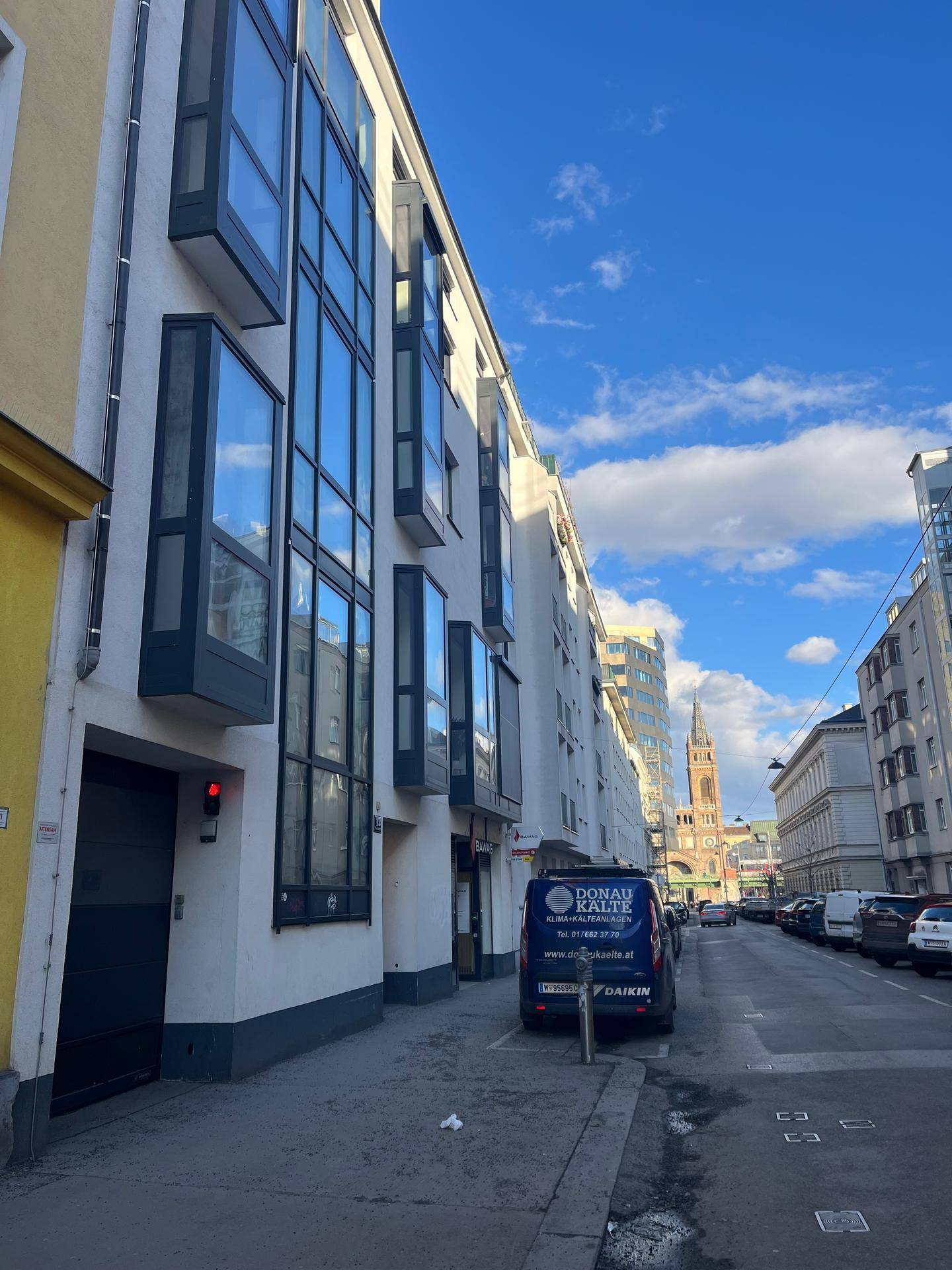 Moderne Wohnfassade mit großen Fenstern und Erkern an einer städtischen Straße unter blauem Himmel.