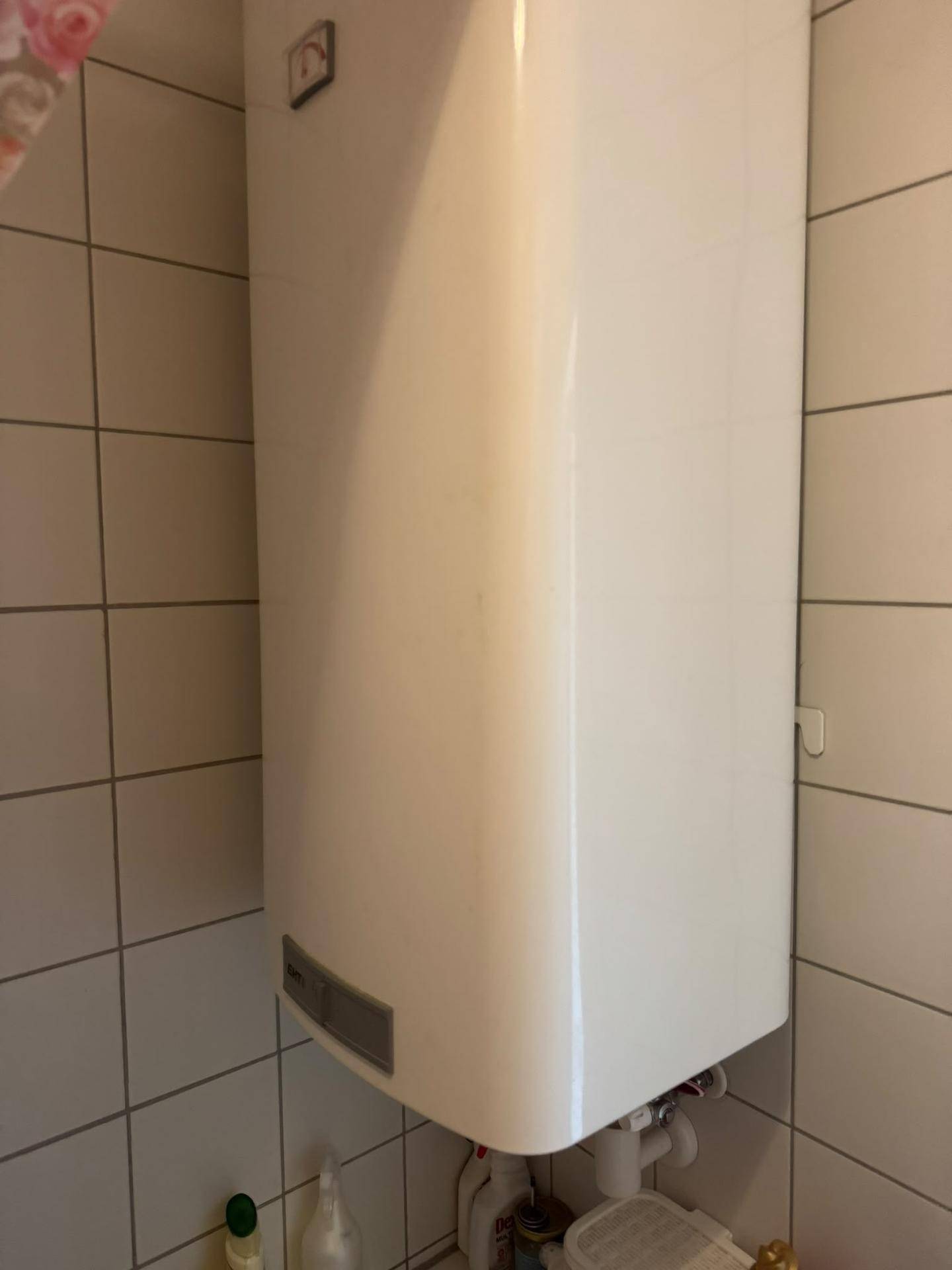 Wandmontierter Warmwasserbereiter in einem gefliesten Raum, möglicherweise Badezimmer oder Hauswirtschaftsraum.