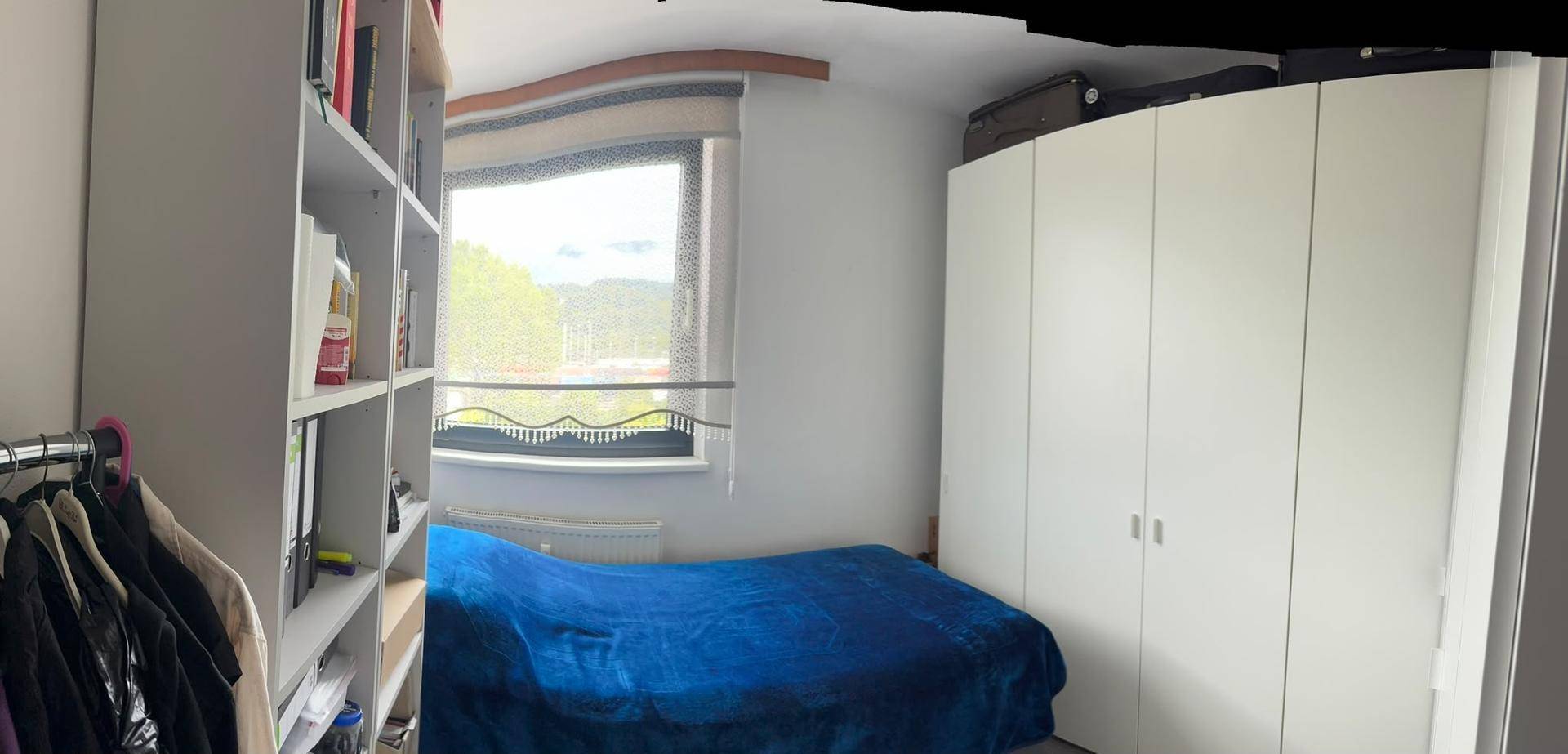 Schlafzimmer mit Bett, großem Kleiderschrank und Fenster mit Blick ins Grüne.