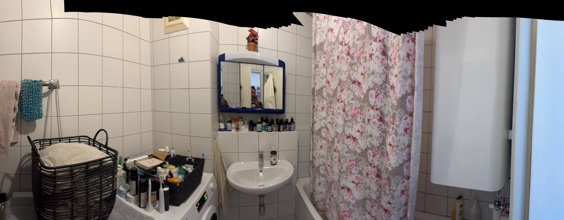 Badezimmer mit Waschbecken, Spiegelschrank, Dusche und Waschmaschine, komplett gefliest.