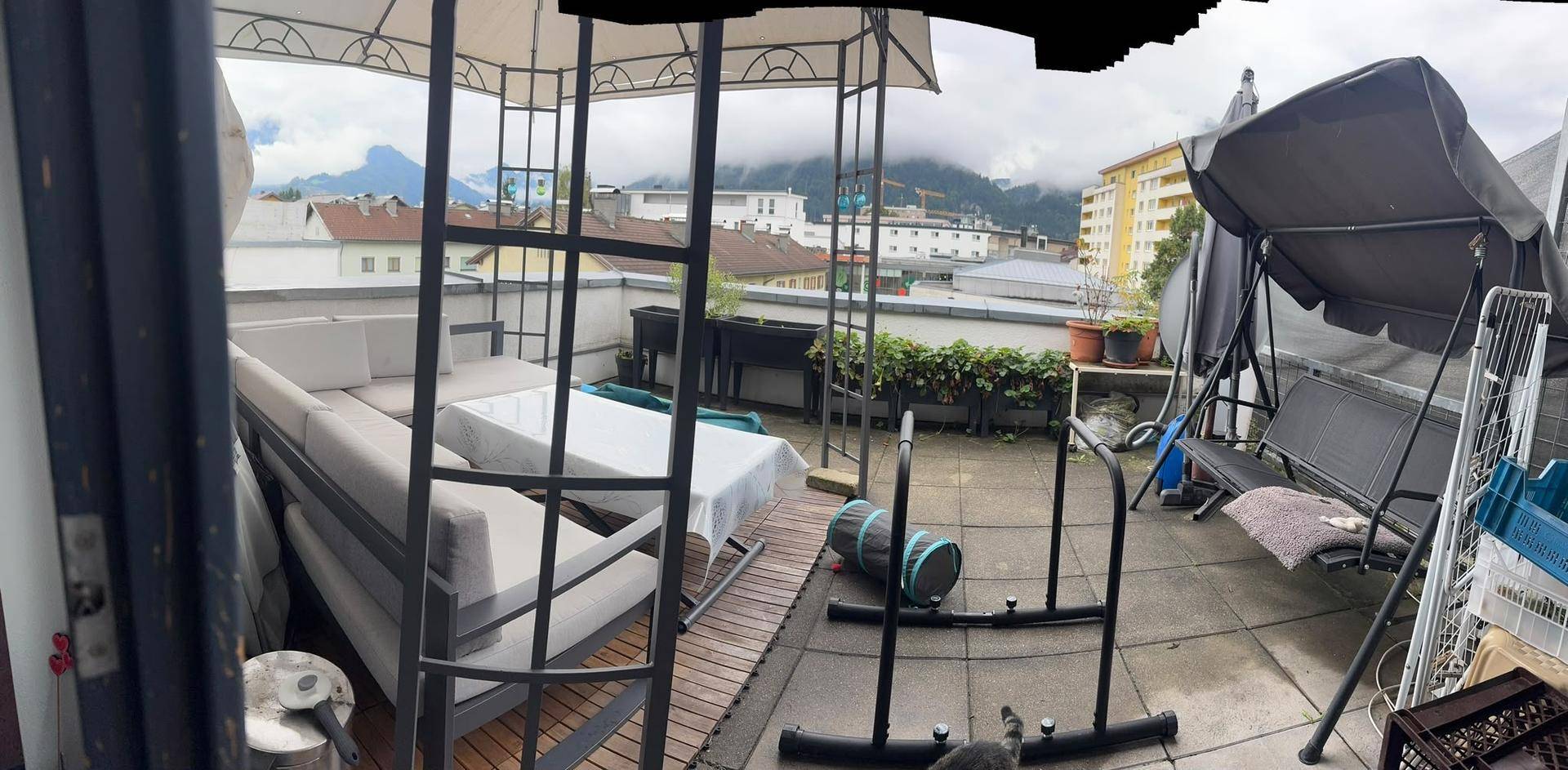Weitläufige Dachterrasse mit Pavillon, Sitzbereich und Trainingsgeräten, umgeben von Stadtblick.