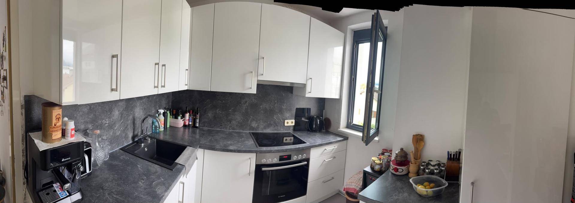 Moderne Küche mit weißen Hochglanzschränken, dunkler Arbeitsplatte und integrierten Geräten.
