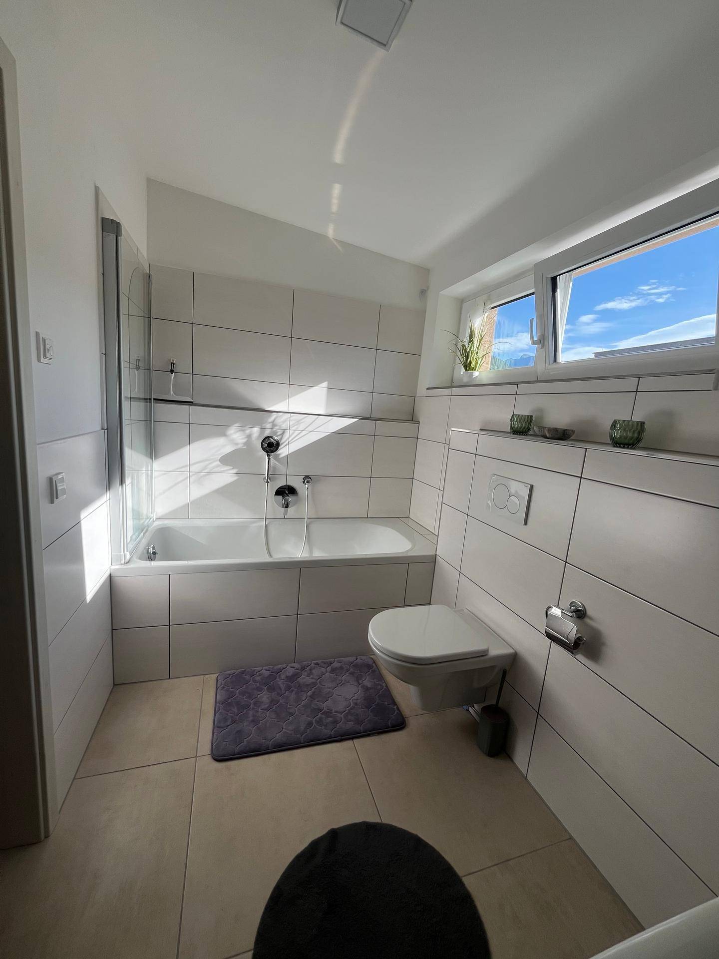 Modernes Badezimmer mit Badewanne, WC und Fenster für Tageslicht.