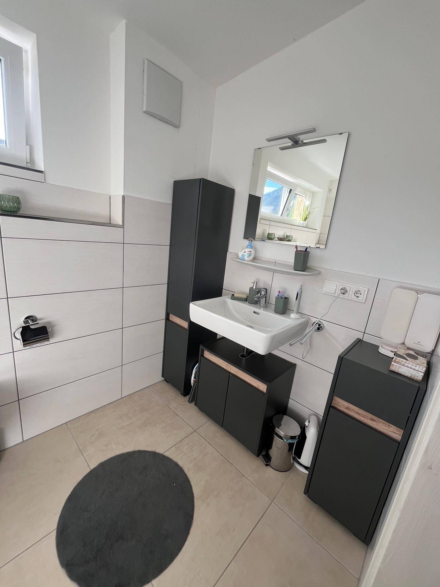 Helles Badezimmer mit Einzelwaschbecken, Spiegelschrank und modernen dunklen Möbeln.