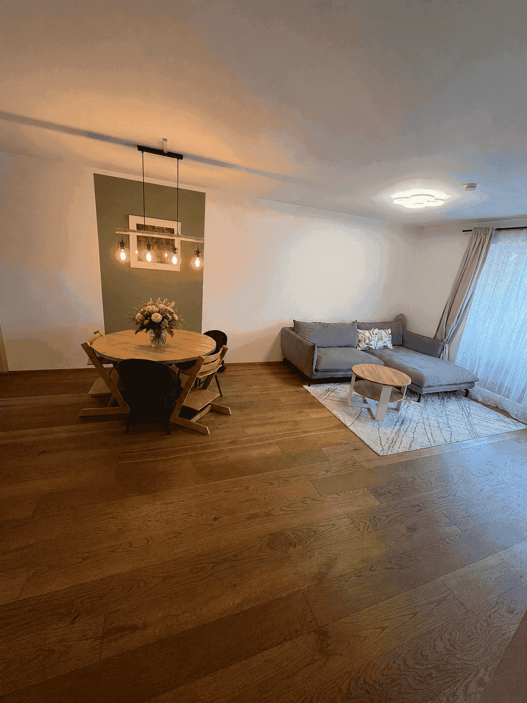 Offener Wohn- und Essbereich mit Holzboden, modernem Esstisch und gemütlichem Sofa.