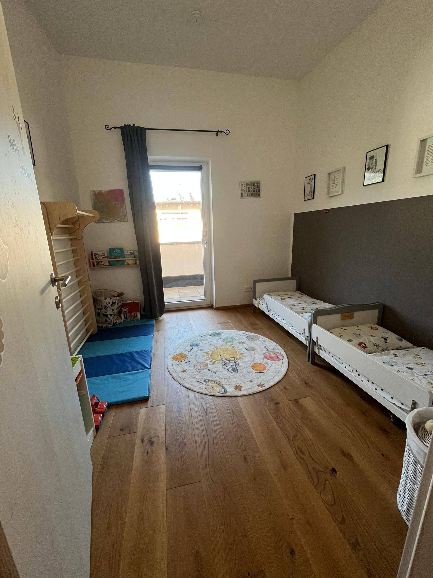Kinderzimmer mit Holzboden, zwei Betten und Zugang zu einem kleinen Balkon.