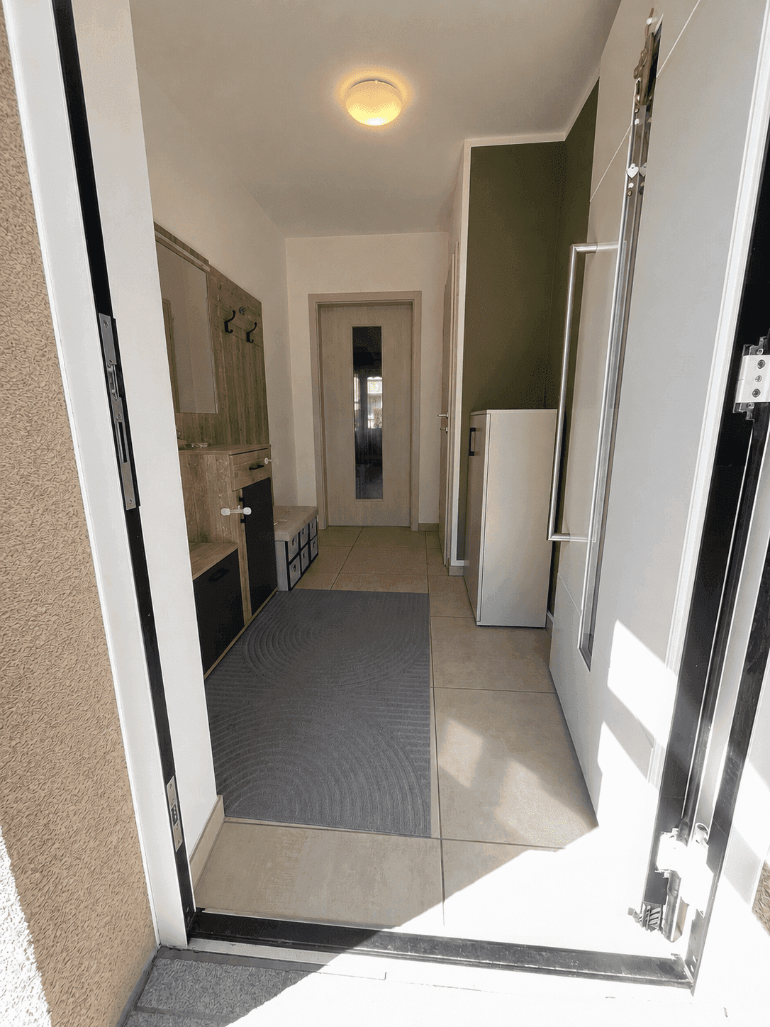Heller Eingangsbereich mit Fliesenboden, Garderobe und moderner Haustür.