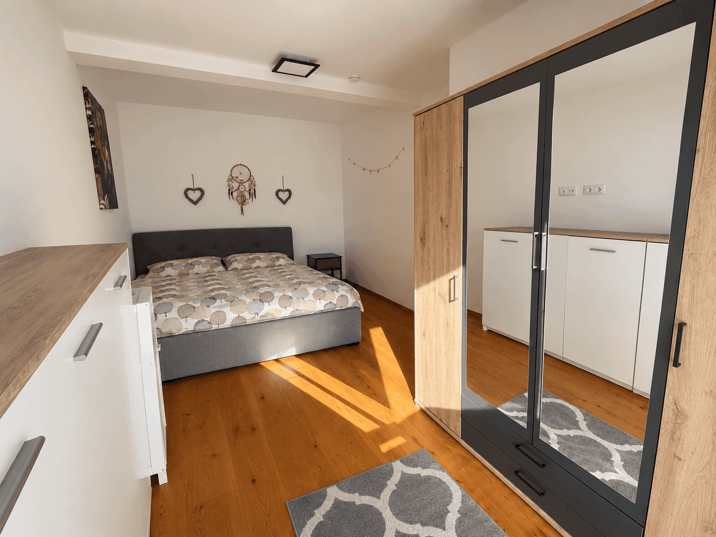 Helles Schlafzimmer mit Holzboden, Doppelbett und großem Spiegelschrank.