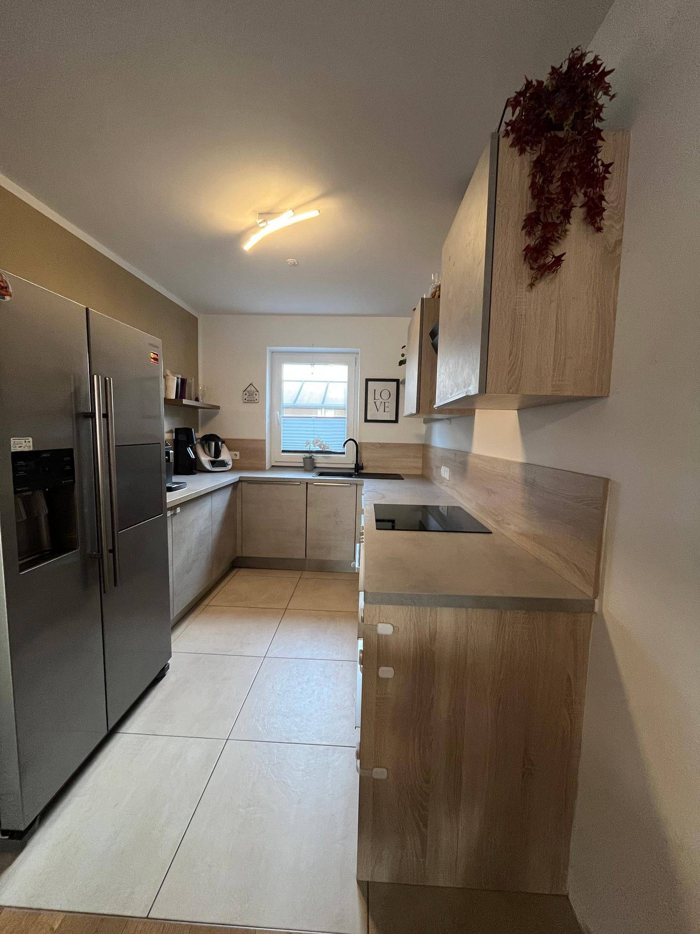 Moderne Küche mit hellen Holzfronten, Fliesenboden und großem Kühlschrank.