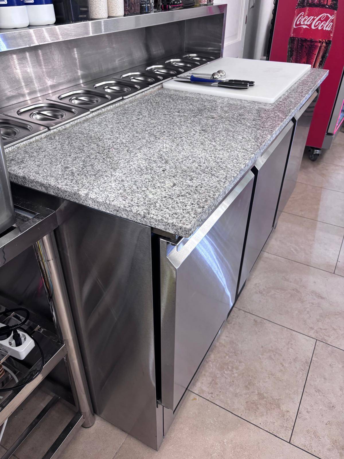 Professionelle Edelstahltheke mit Granitarbeitsplatte und integrierten Behältern für die Zubereitung.