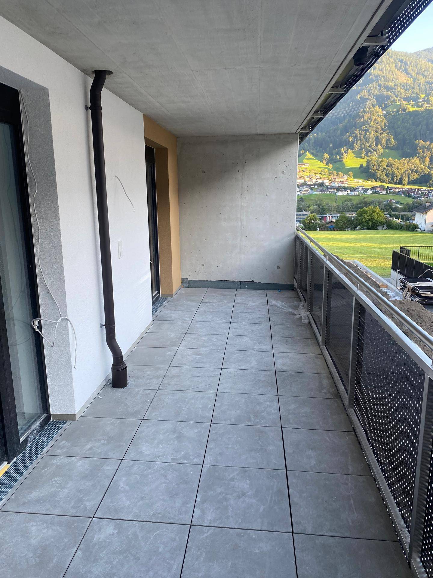 Geräumiger Balkon mit modernen grauen Fliesen, Betonoptik und weitem Blick auf die Berge und das Tal.