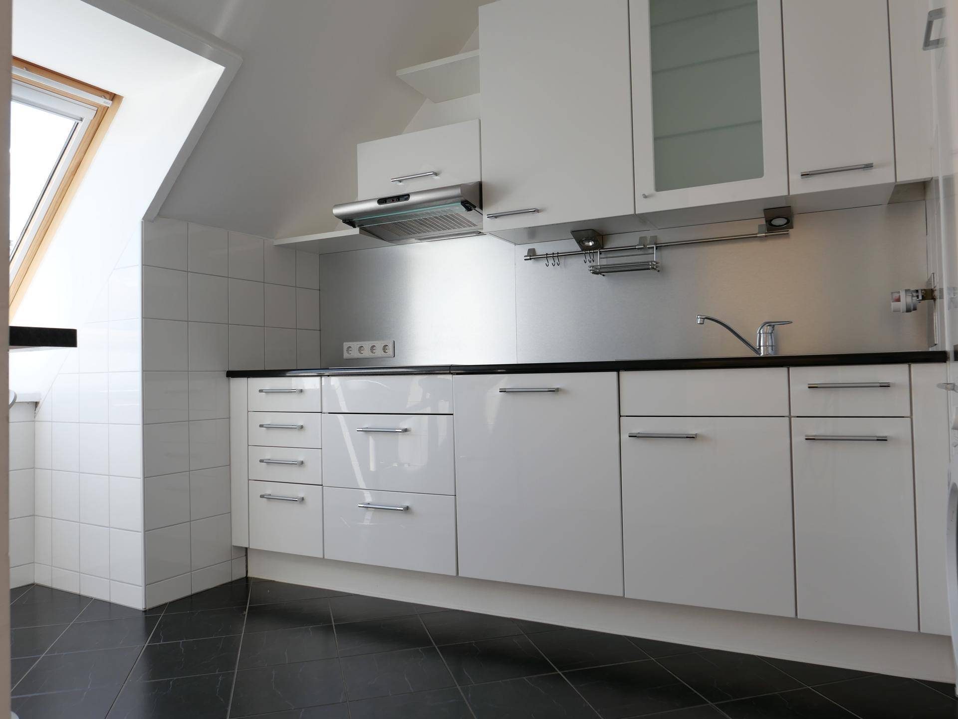 Moderne Küche mit weißen Hochglanzschränken, dunkler Arbeitsplatte und Dachfenster.