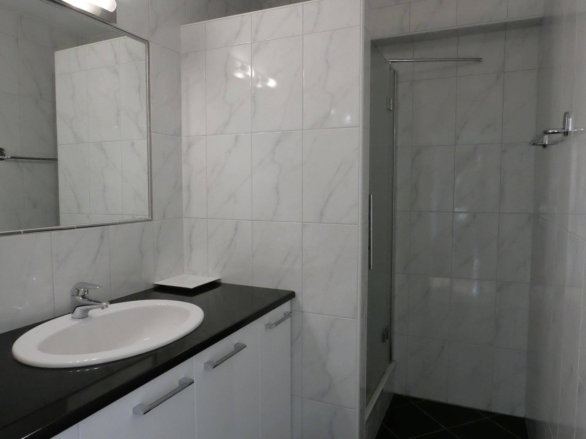 Modernes Badezimmer mit weißen Fliesen, Einzelwaschbecken und Duschkabine.