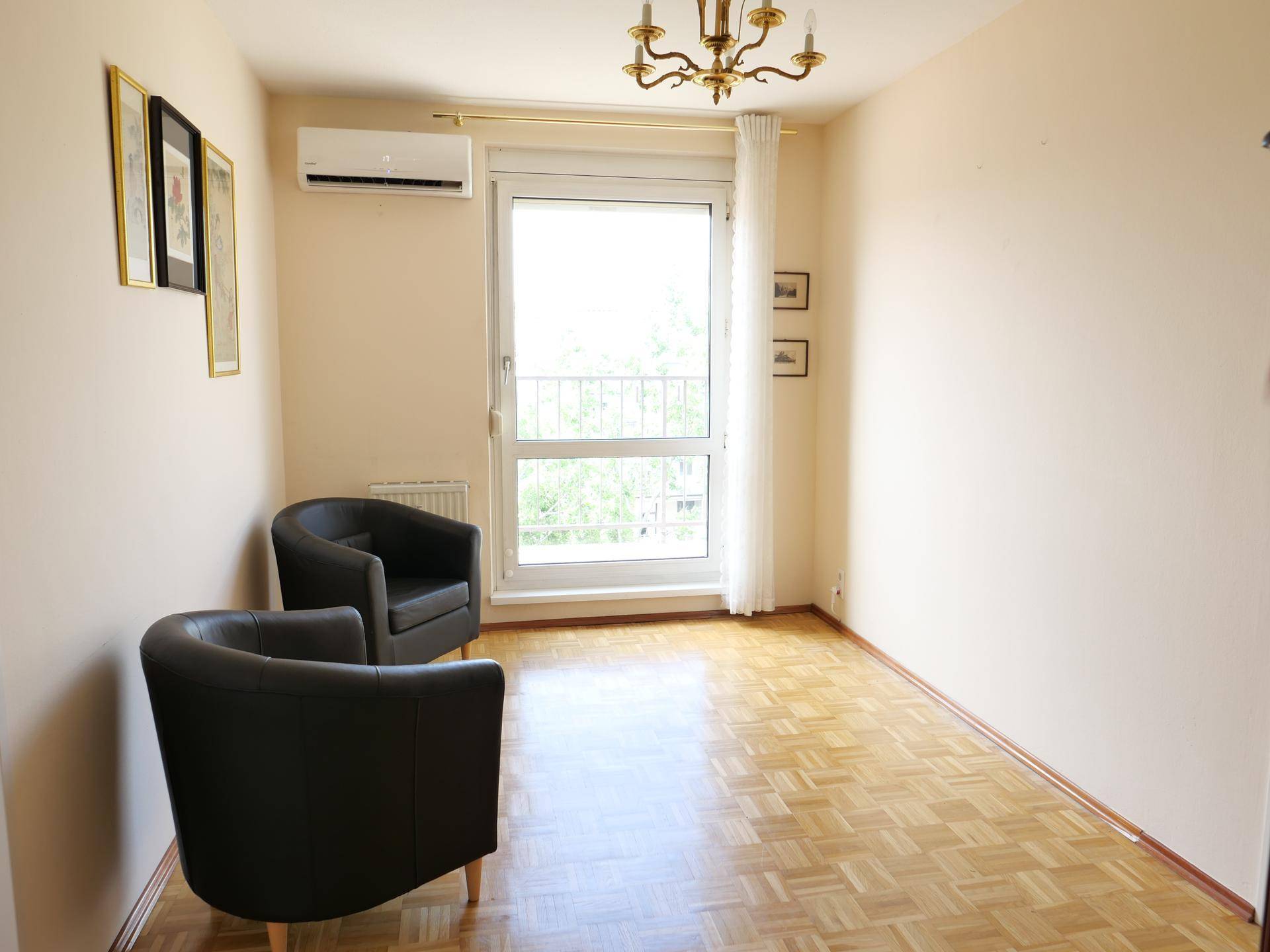 Heller Raum mit Parkettboden, Klimaanlage und Zugang zu einem französischen Balkon.