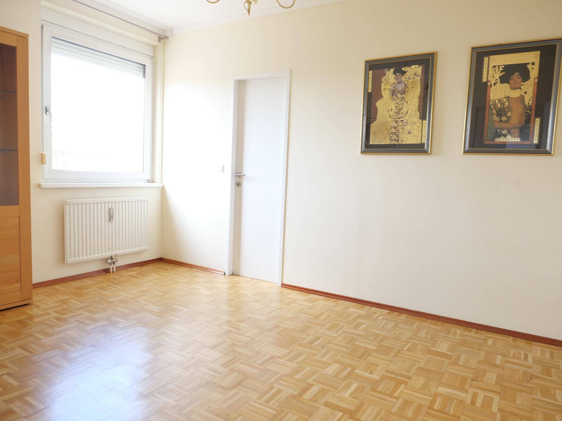 Freundlicher Raum mit Parkettboden, Fenster mit Rollladen und Heizkörper.