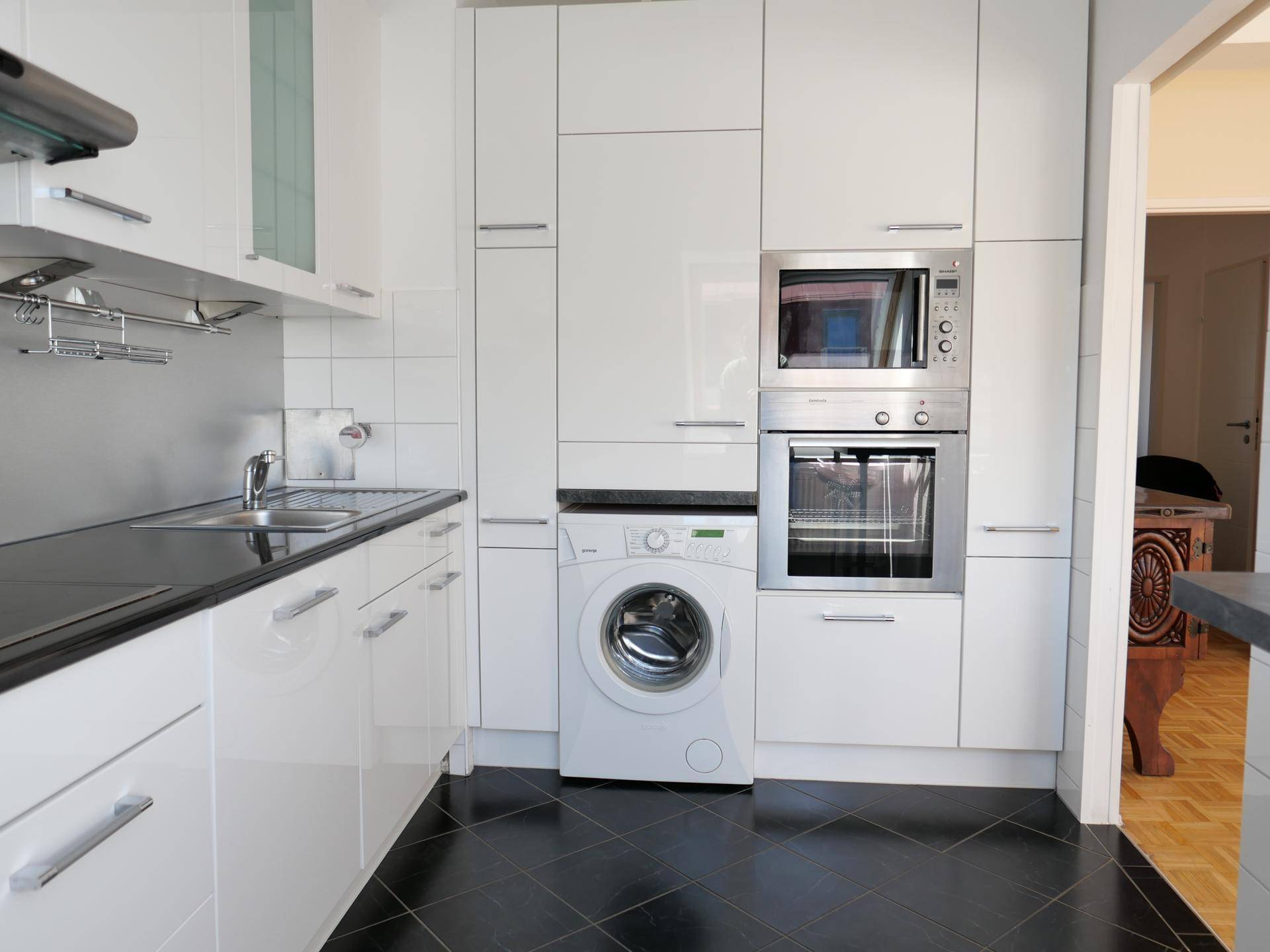 Funktionale Küche mit integrierten Geräten, Waschmaschine, Backofen und Mikrowelle.