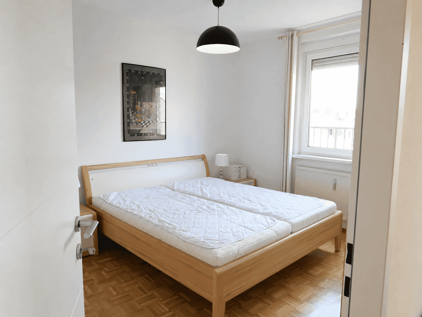 Gemütliches Schlafzimmer mit Doppelbett, Parkettboden und Fenster für natürliches Licht.