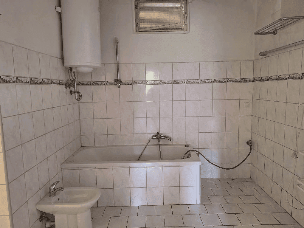Gefliestes Badezimmer mit Badewanne, Bidet und Warmwasserboiler an der Wand.